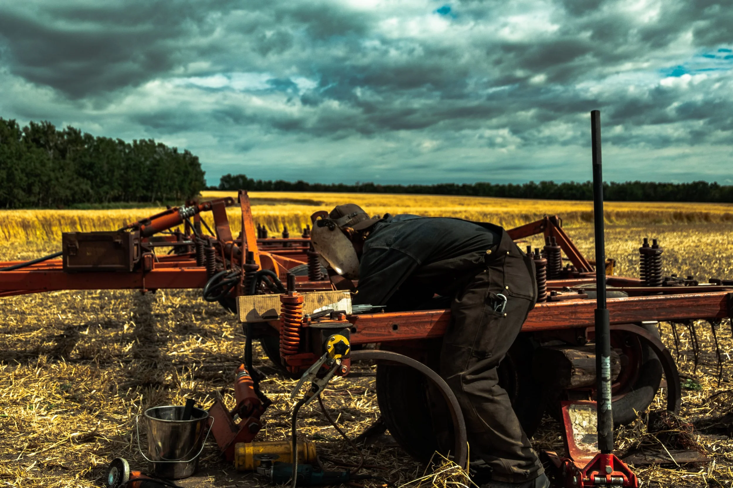 A person working on agricultural machinery in a field under a cloudy sky.