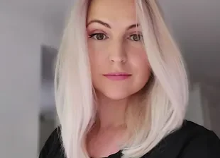A woman with blonde hair and a slight smile, wearing a black top.