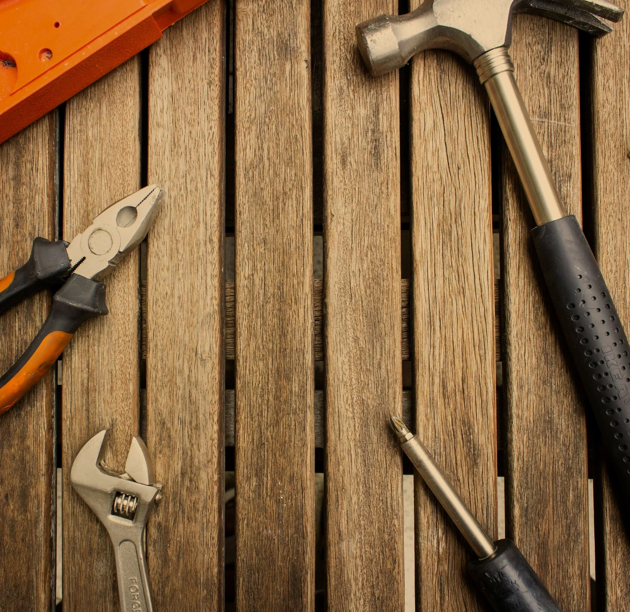 A wooden surface with various tools placed on it, including a pipe wrench, a hammer, and a cordless screwdriver. Drywall Repairs , New Fence , Exterior Repairs , Fascia Painting , Door Painting