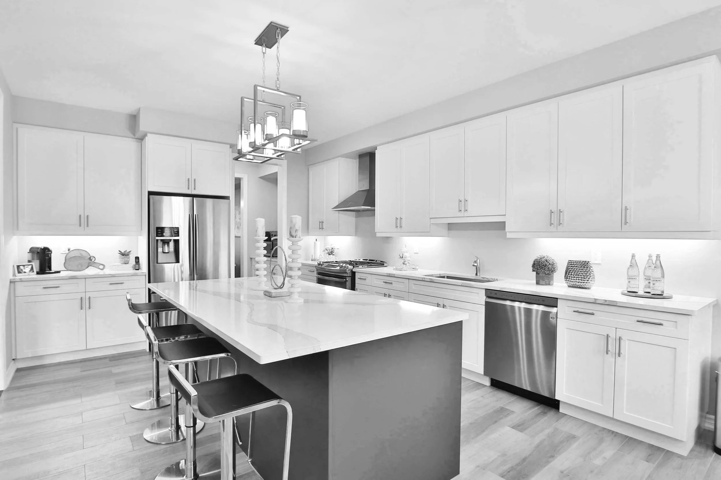 Modern kitchen with white cabinets, stainless steel appliances, a large island with white countertop, and pendant lighting fixture. Interior Renovations , Kitchen remodel , Wall Painting , New Countertops , New flooring , Replace Light Fixture ,