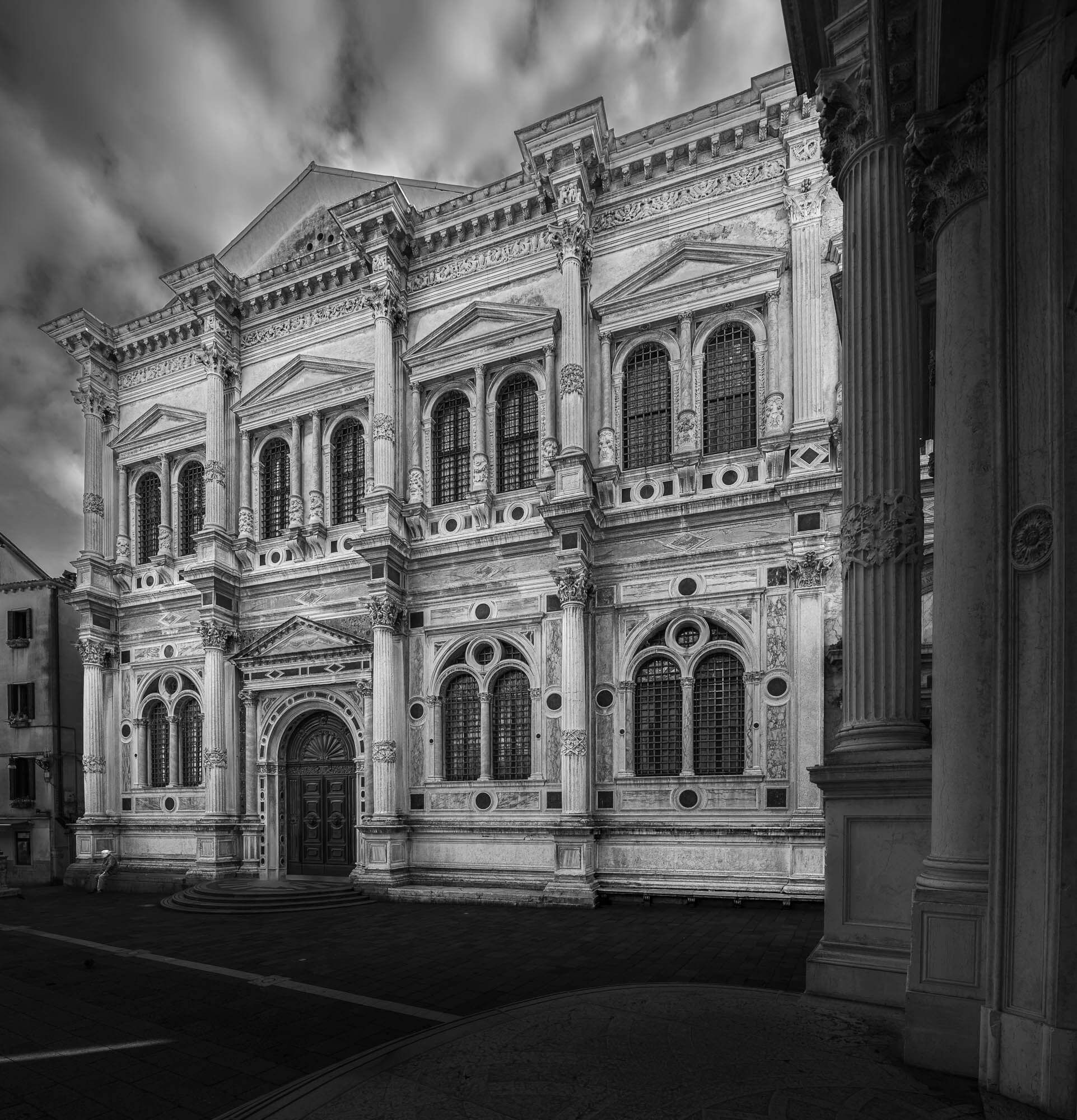 Black and white photo of a historic building with ornate architectural details, columns, and arched windows, set against a cloudy sky.