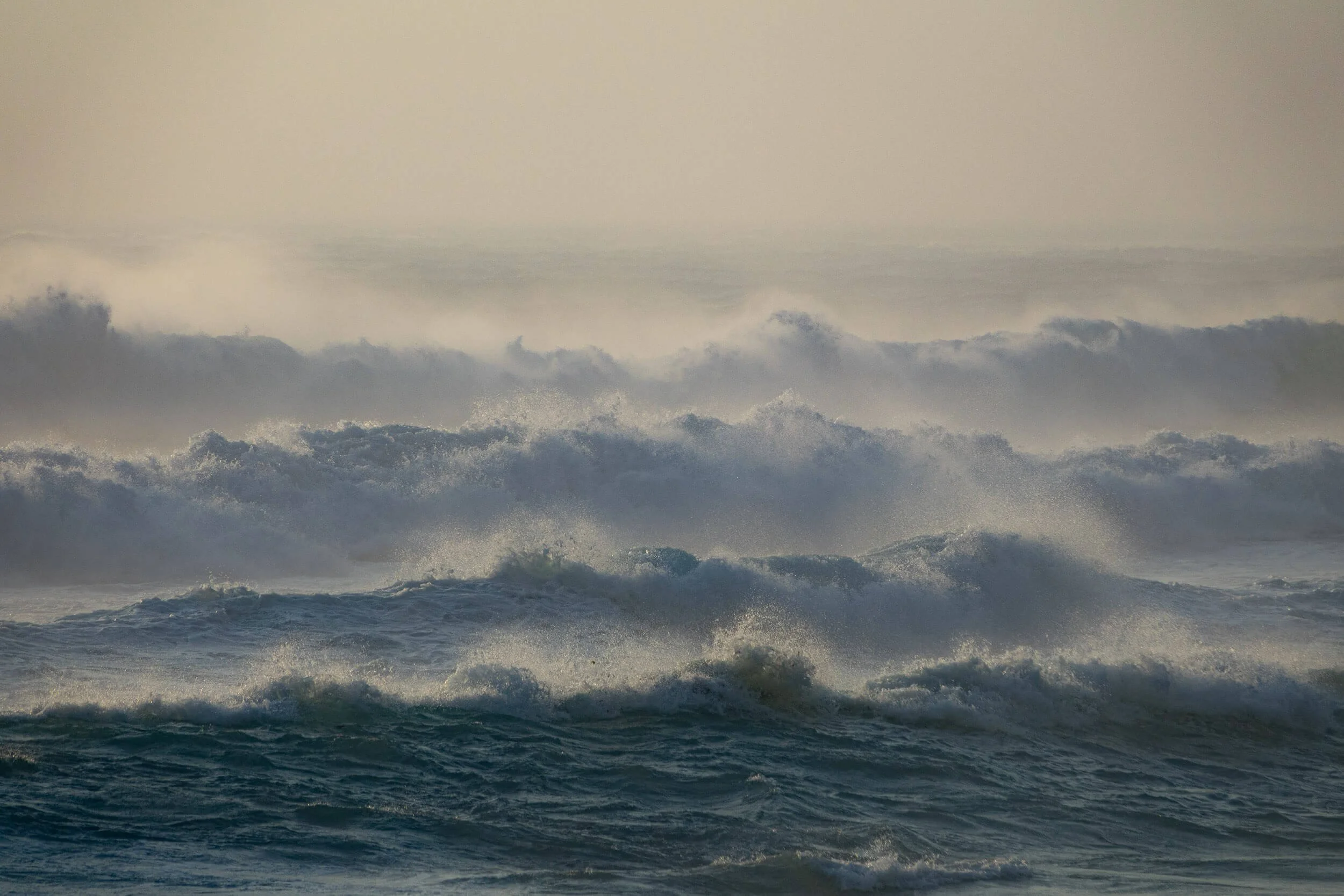Ocean waves crashing with high sea spray and foam, under an overcast sky.