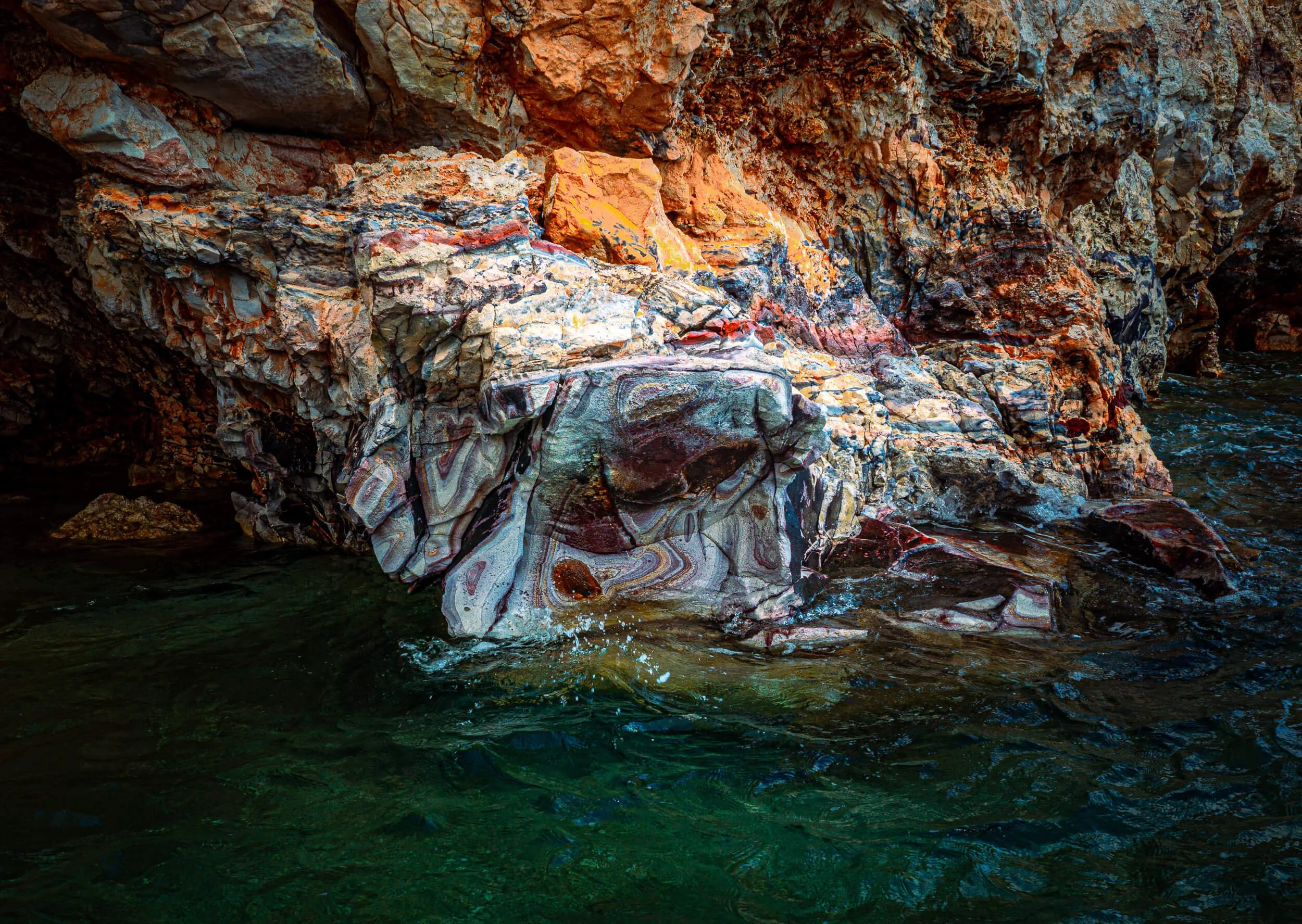 Colorful layered rocks along a body of water at a rocky shoreline.
