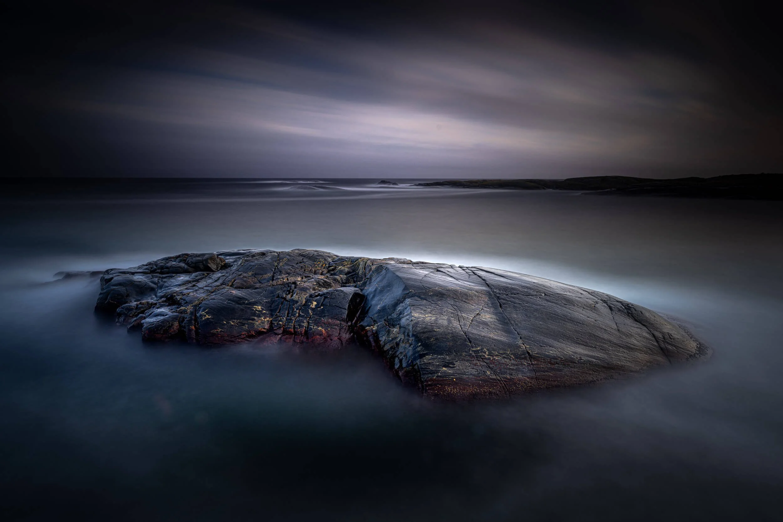 Long exposure photo of a rocky shoreline at night with clouds and ocean waves