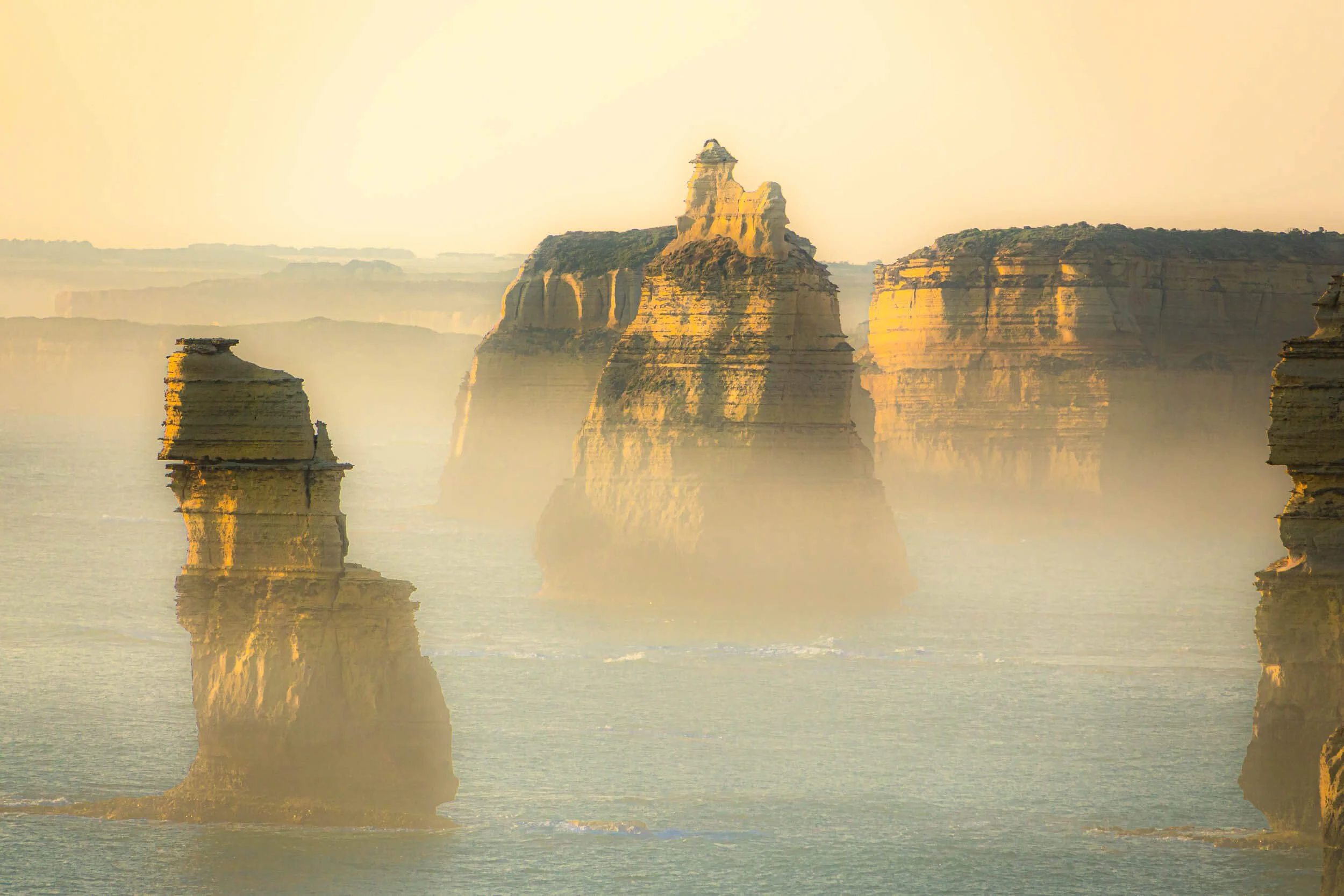 Famous limestone rock formations at sunrise or sunset with a sky filled with soft yellow and orange hues reflected on the calm water below.