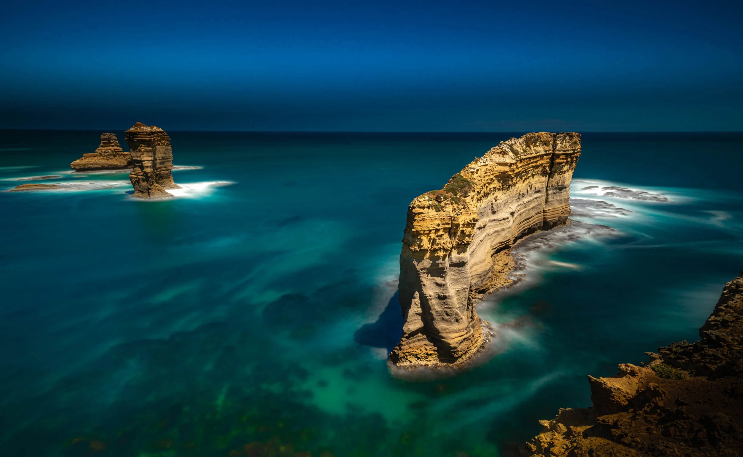 Cliffs on a rocky coastline with blue ocean water and dark sky.