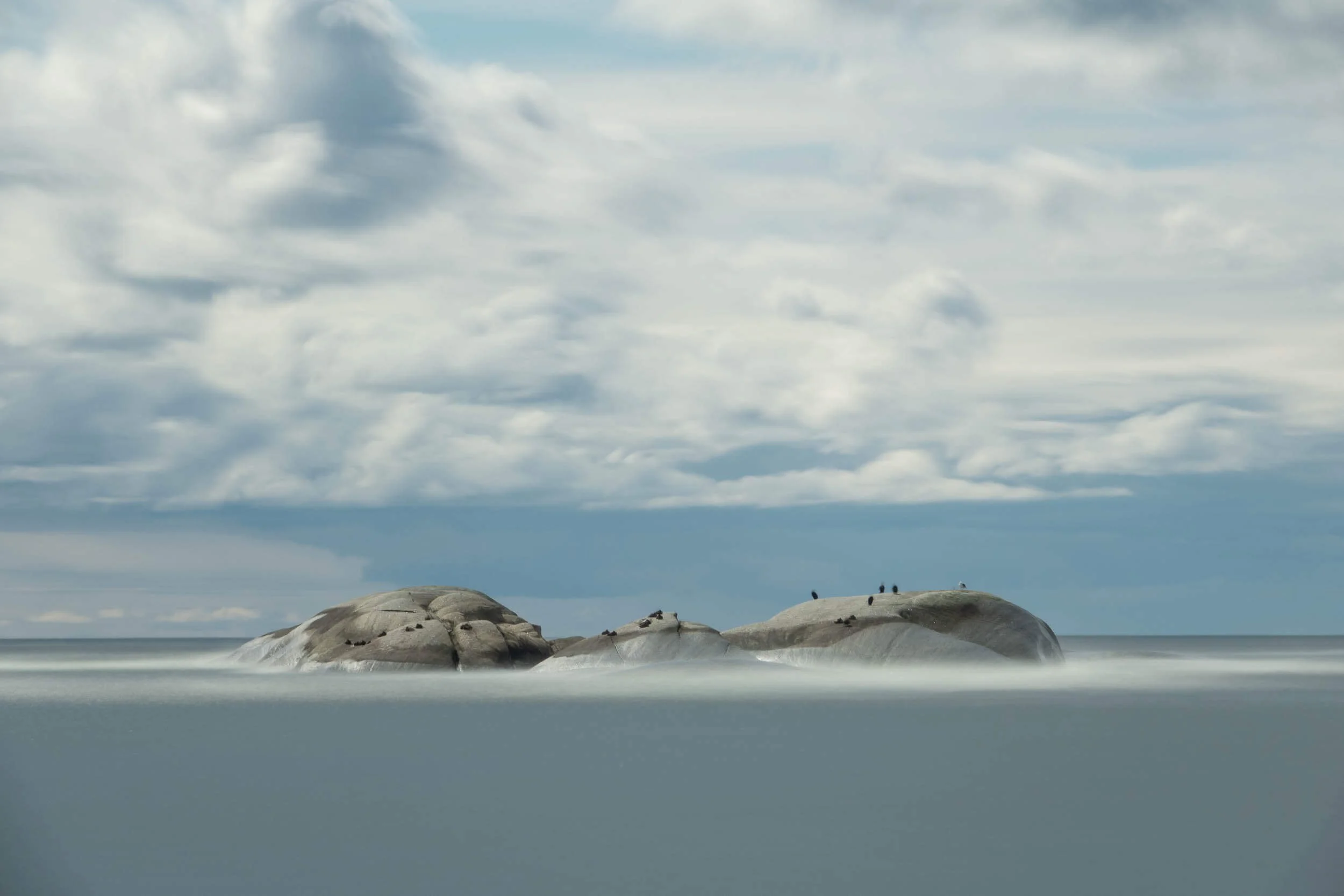 Large rocks on a beach with a cloudy sky overhead.