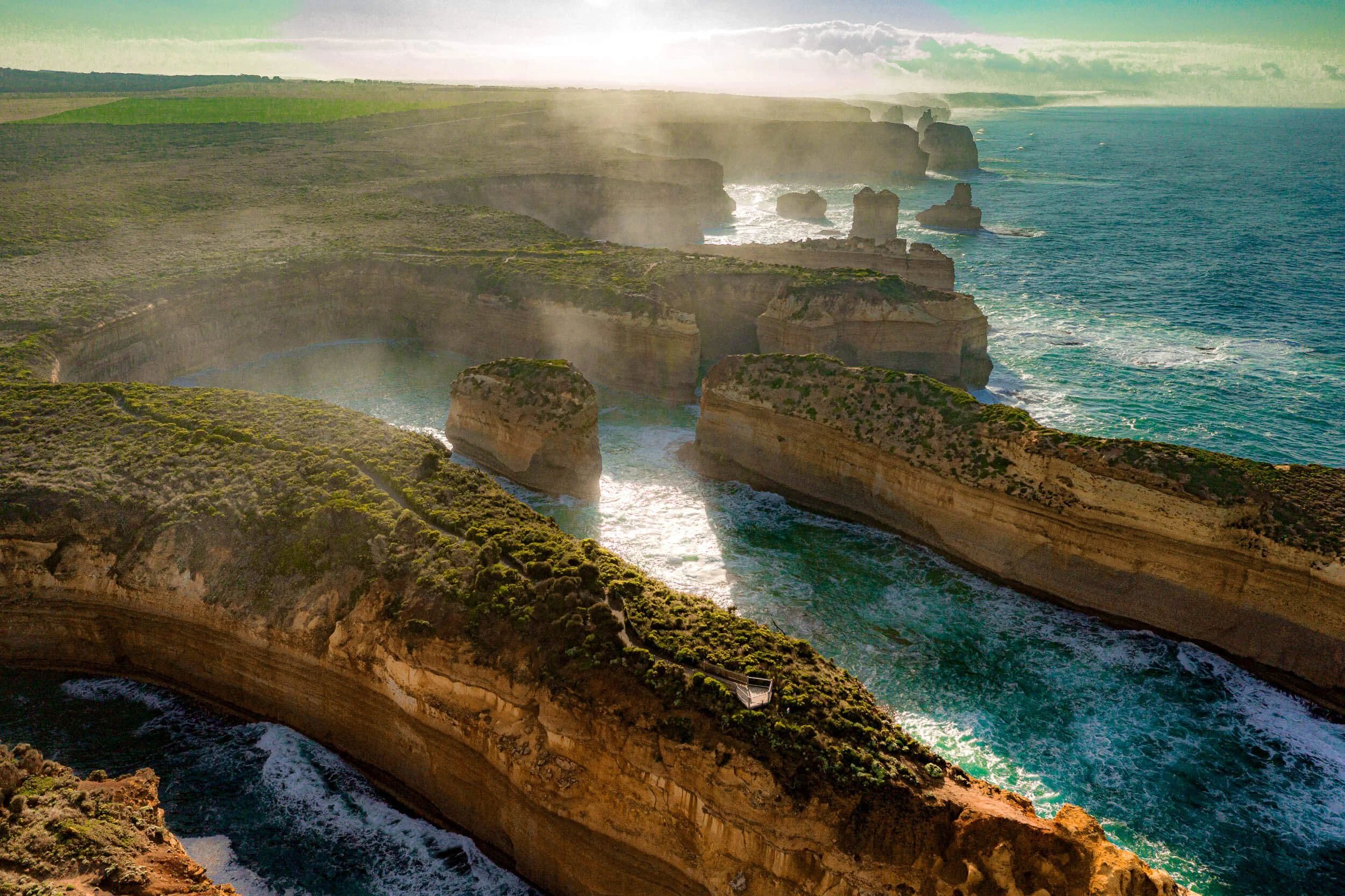 Aerial view of the Cliffs of Moher along the Atlantic Ocean in Ireland, with steep cliffs, green grassy areas, and crashing waves below.