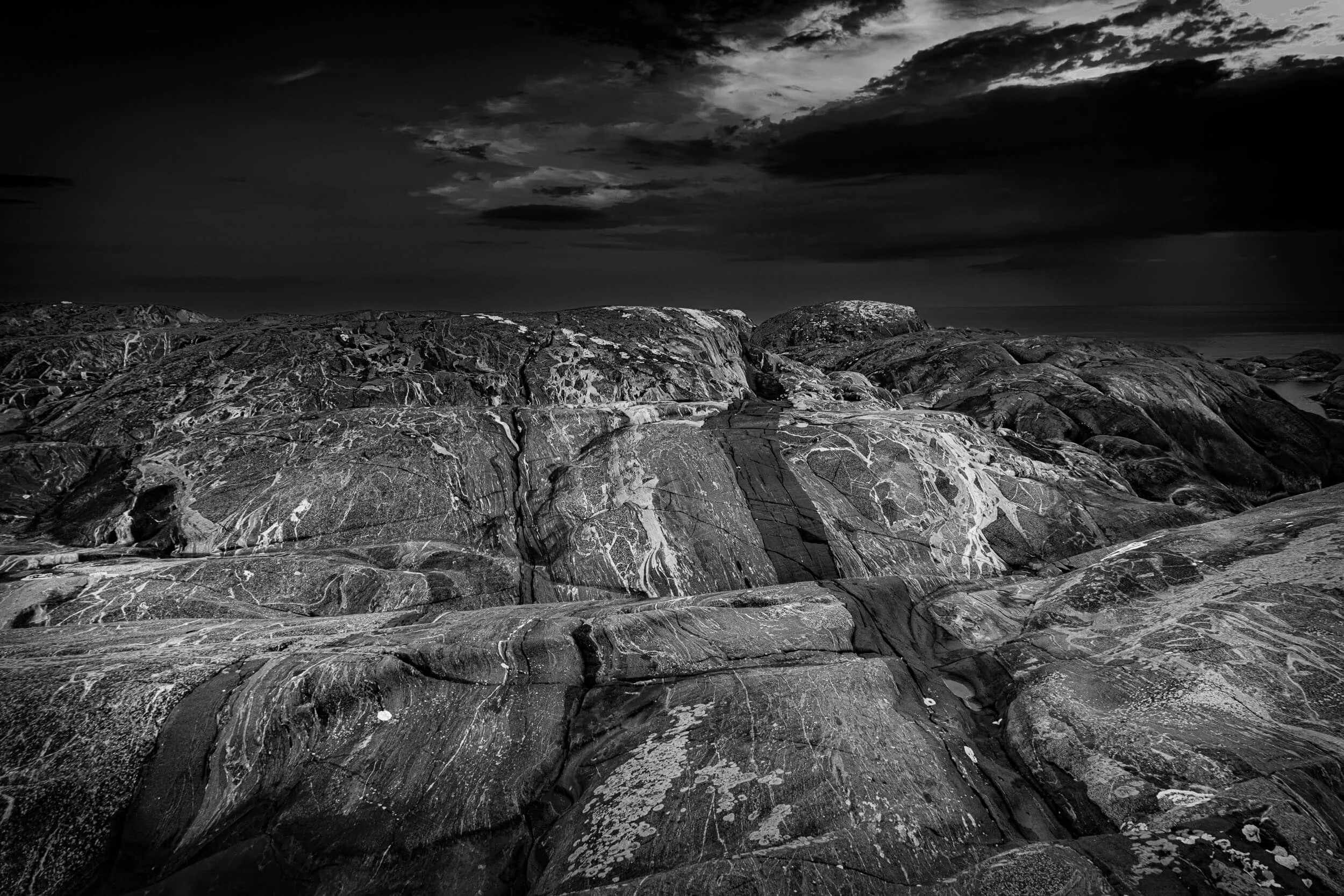 Black and white photograph of rocky shoreline under dark, cloudy sky.