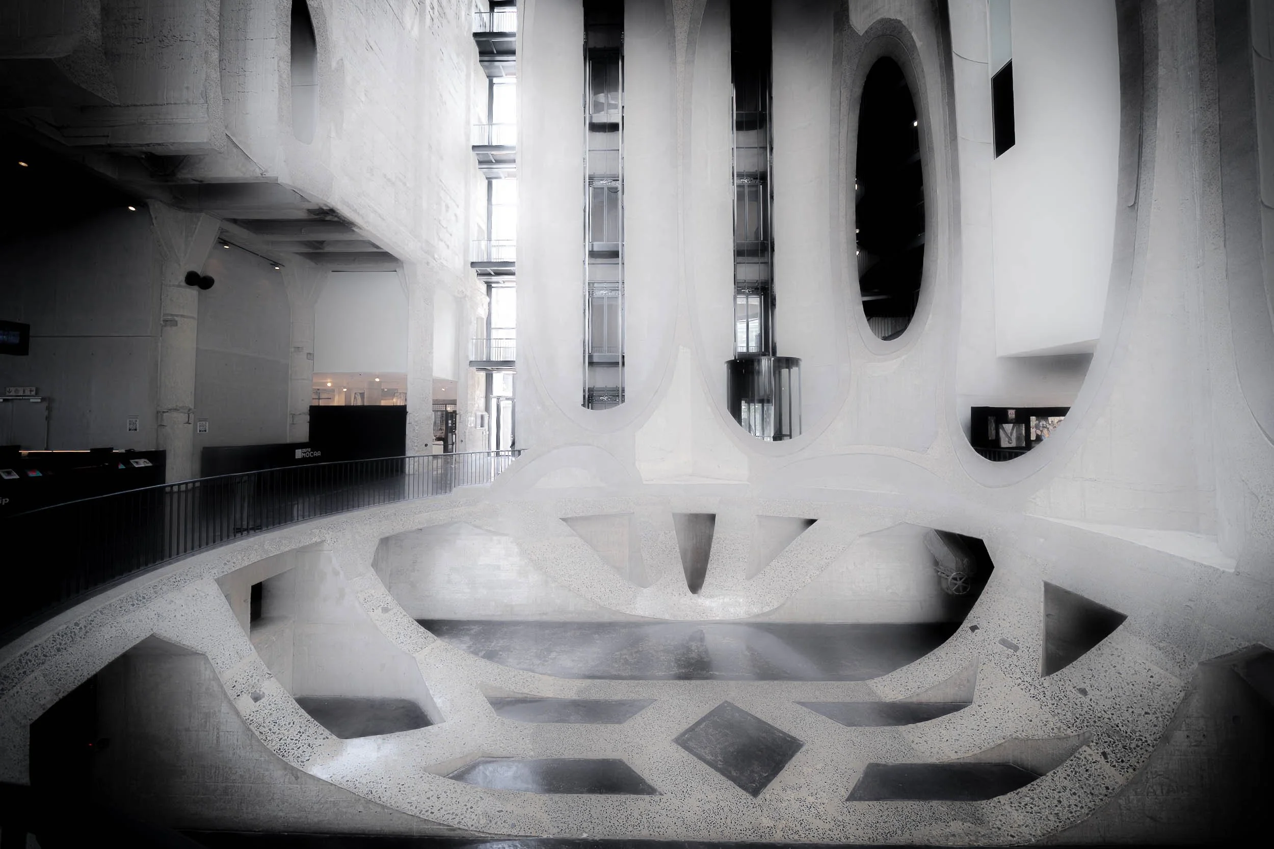 Interior view of a modern building with abstract architectural design, featuring curved concrete walls, metal elevators, and large openings.