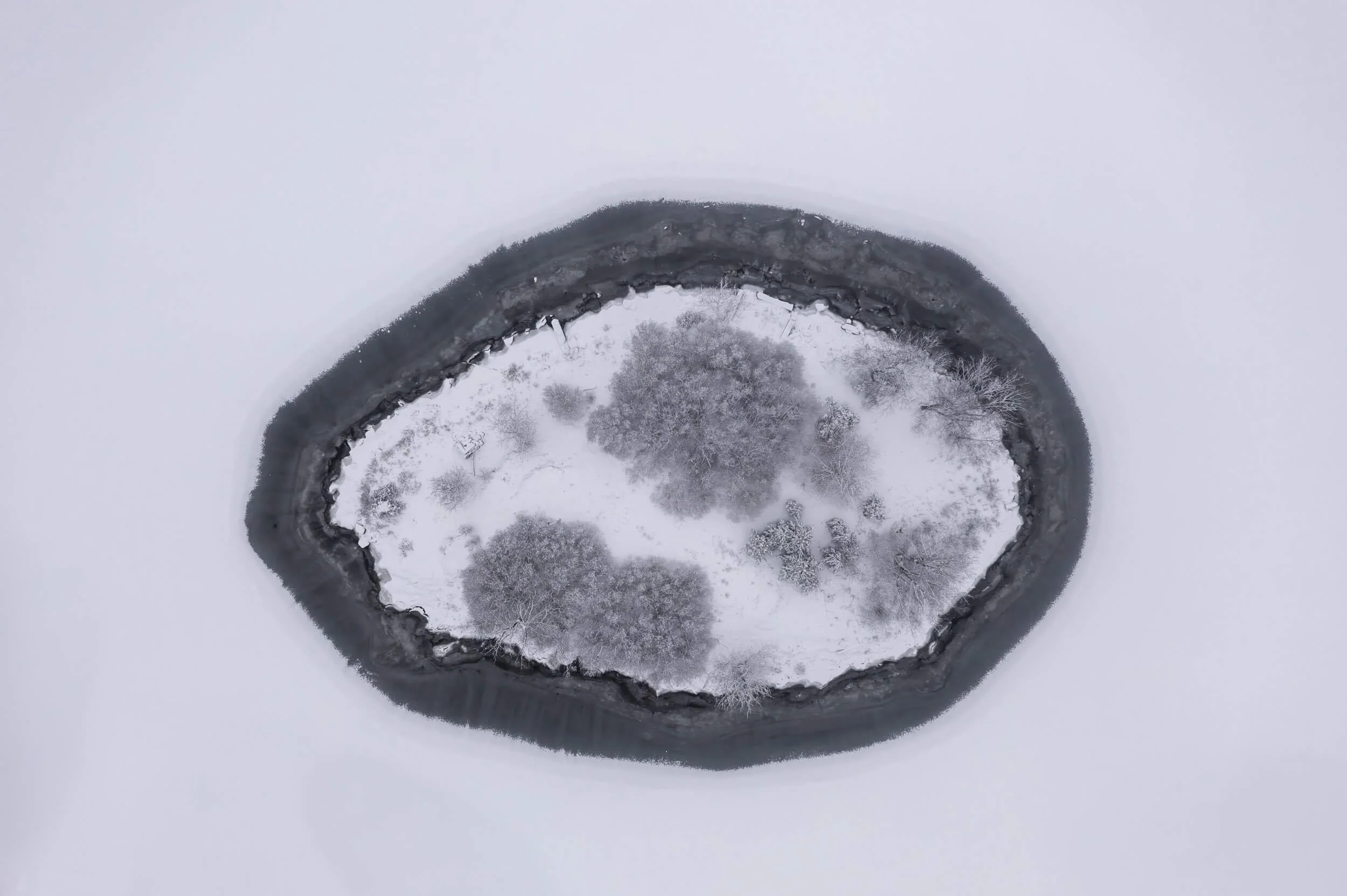A snowy landscape with a circular clearing, surrounded by trees and a winding road.