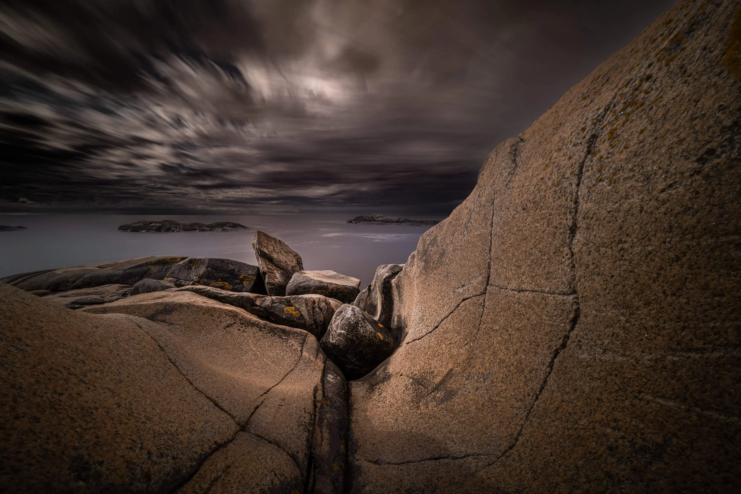 Large rocks and boulders on a beach with a dark, cloudy sky overhead.