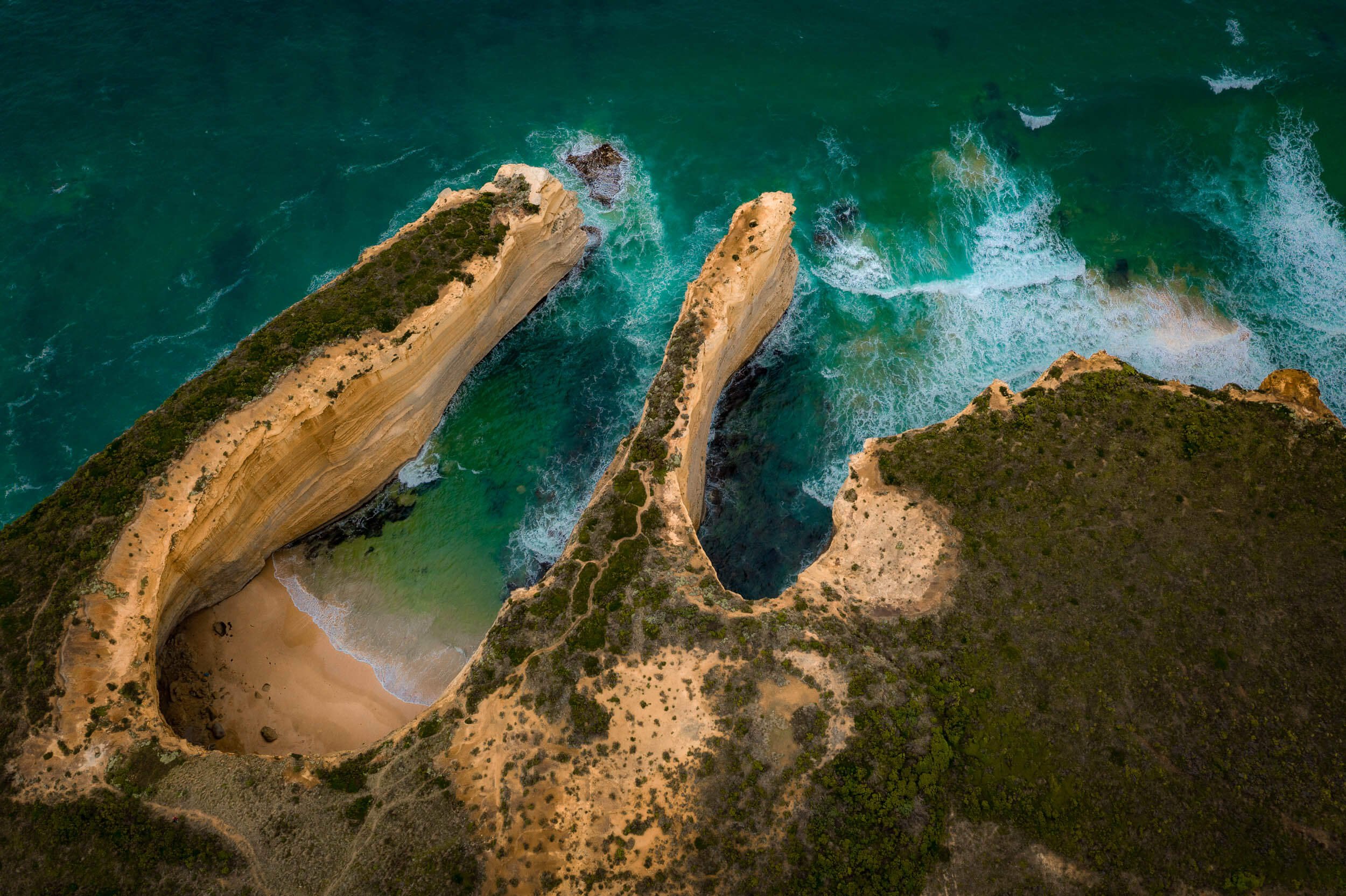 Aerial view of a coastal landscape with a large natural rock formation and a beach, surrounded by ocean waves.