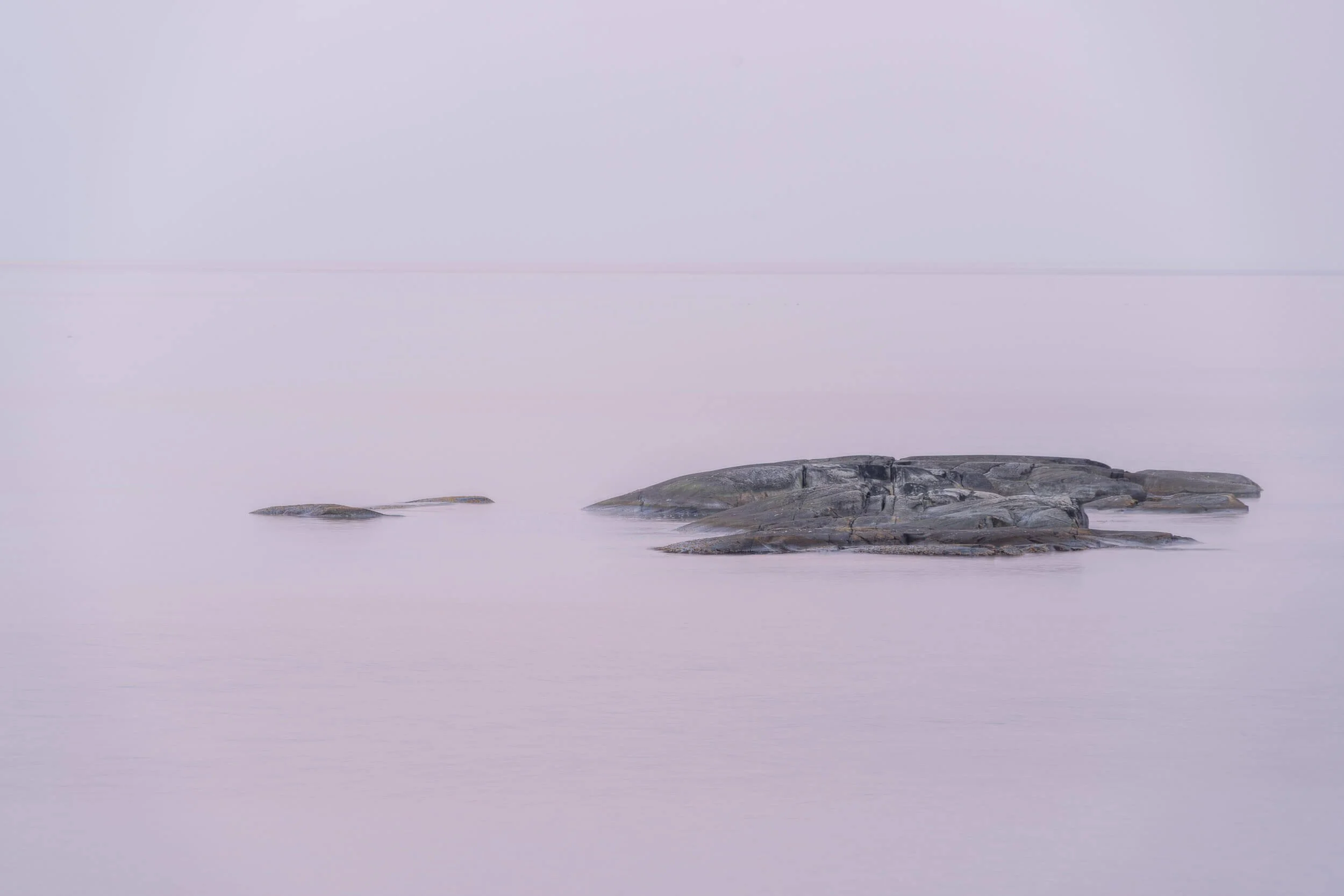 Calm, foggy lakeside scene with rocks in the water, minimal color palette, and smooth water surface.