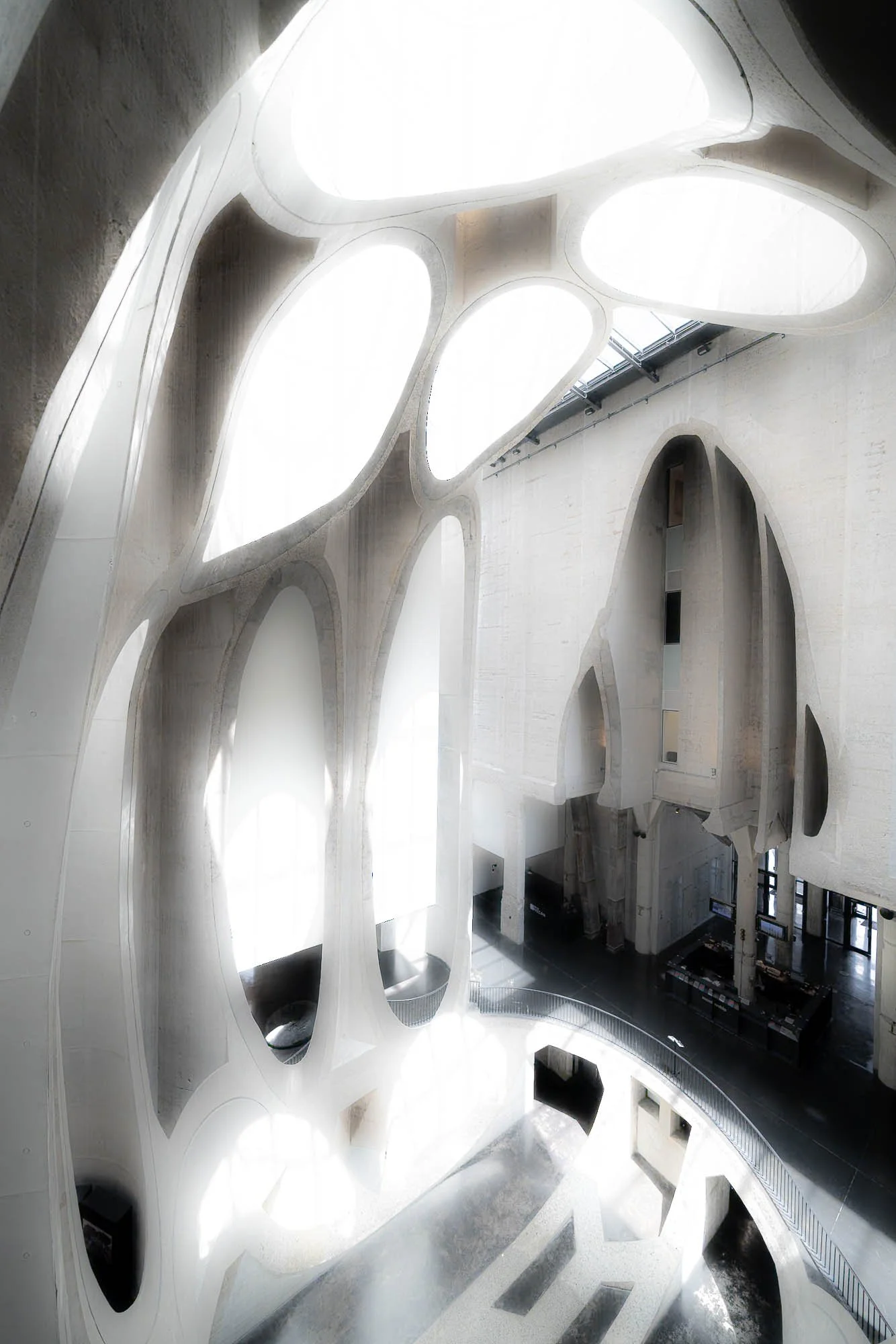 Interior view of the Museum of the Second World War in Gdańsk, Poland, showcasing modern architecture with curving white walls, oval and irregular openings, and natural light streaming through large skylights.