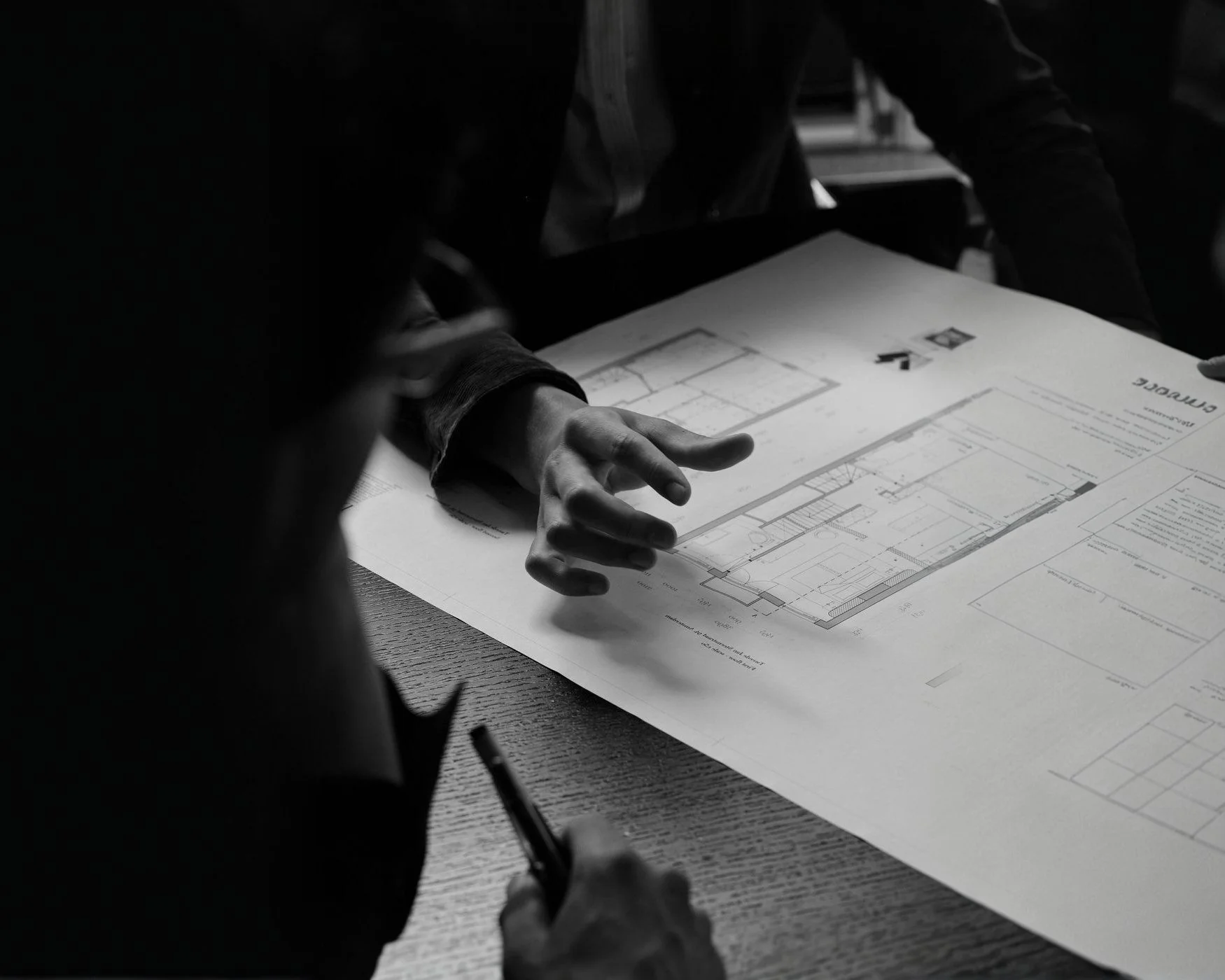 A person reviewing architectural blueprints on a table, with part of the person and the drawing visible in a black and white photo.