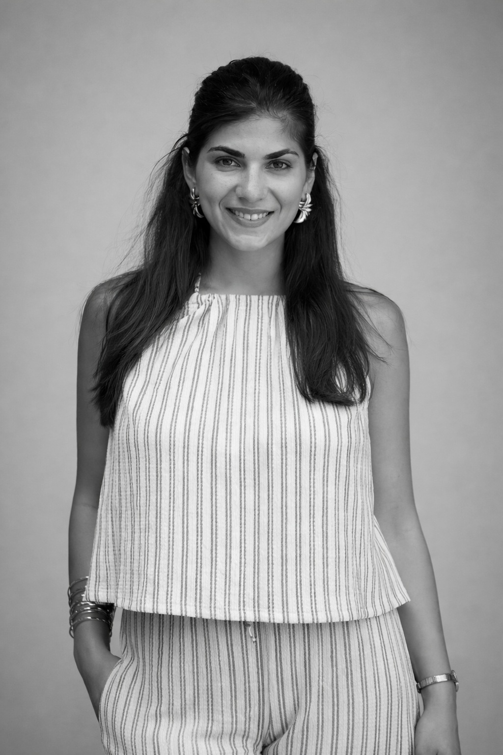 Black and white portrait of a young woman with long dark hair, wearing a sleeveless striped top and matching striped pants, smiling at the camera against a plain background.