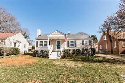 Front view of a house with steps leading to a porch, American flag, and a lawn in the foreground.