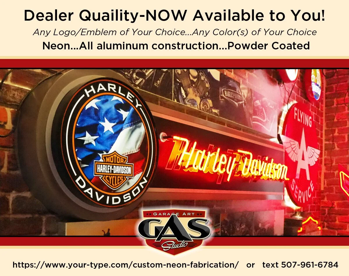 Neon sign with Harley Davidson logo, featuring a American flag and motorcycle helmet, in a garage or auto service shop with a brick wall background.