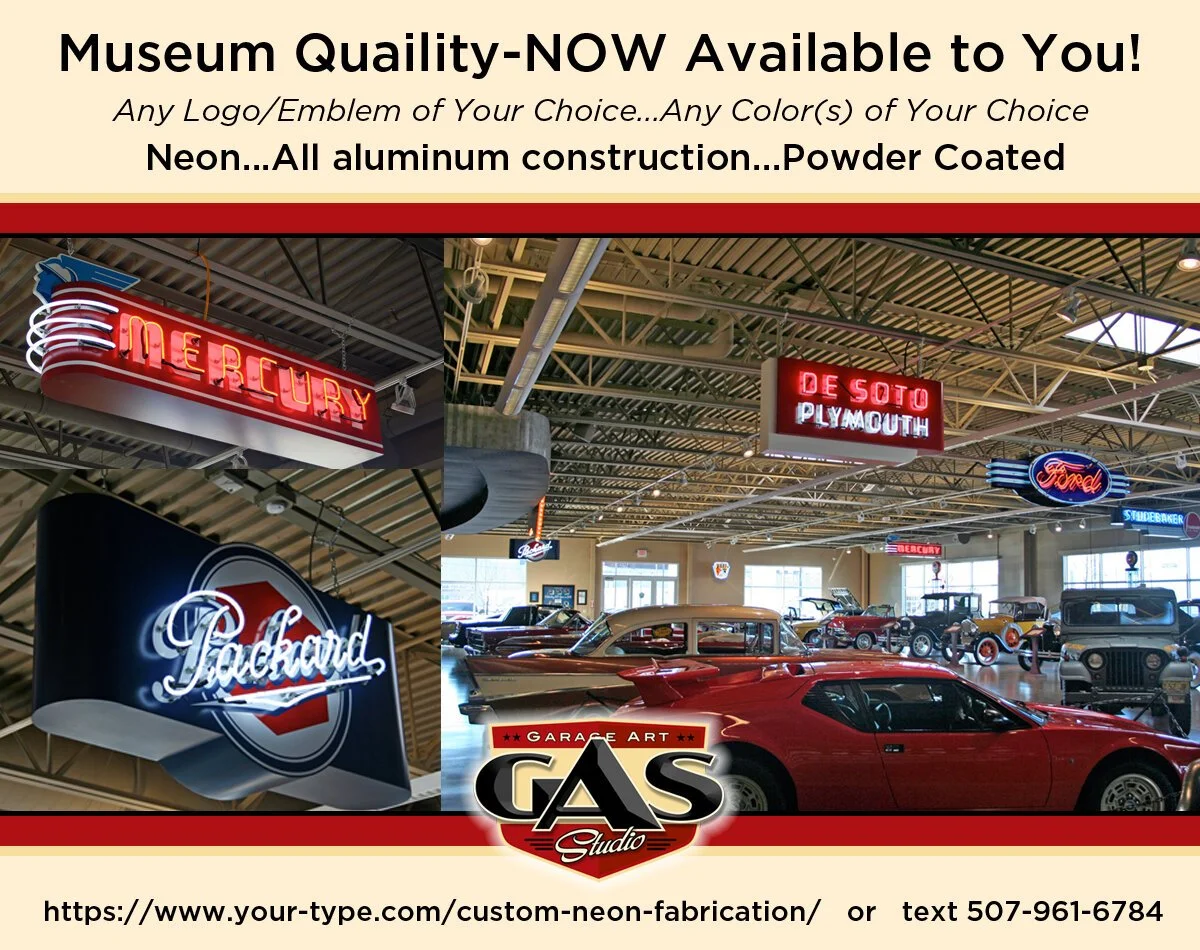 Collection of neon signs for Mercury, Packard, De Soto Plymouth, and Ford, displayed above vintage cars inside a showroom or museum, with visible ceiling and lighting fixtures.