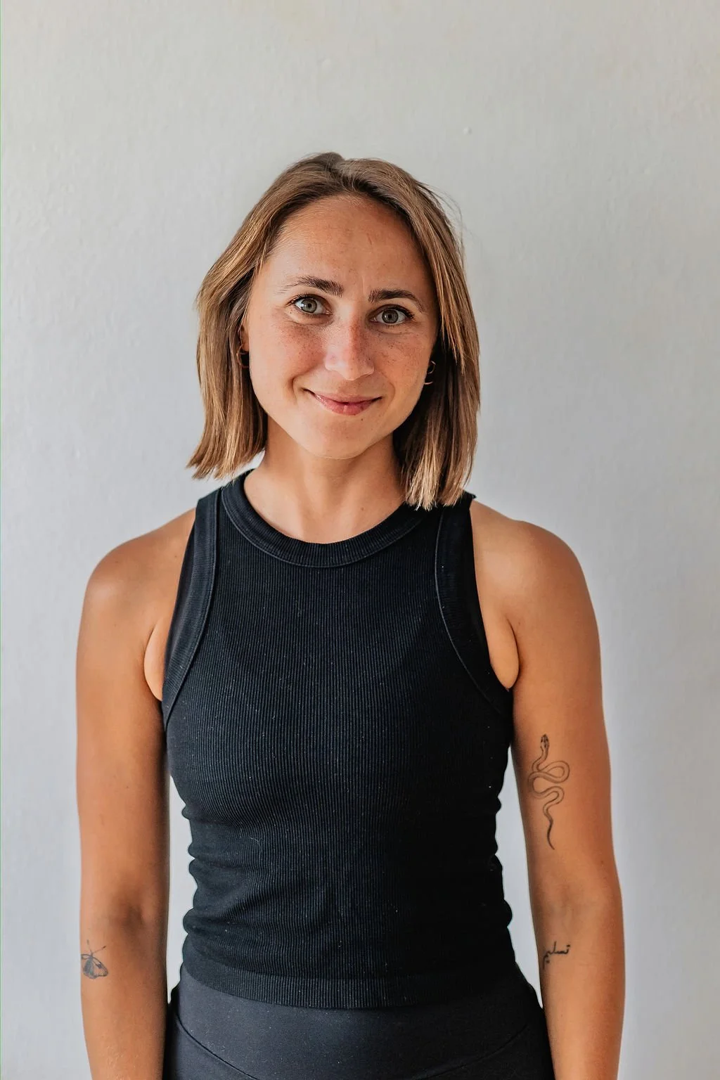 Liana in portrait posture, wearing black Yoga clothes, her hair down. Smiling to the camera.