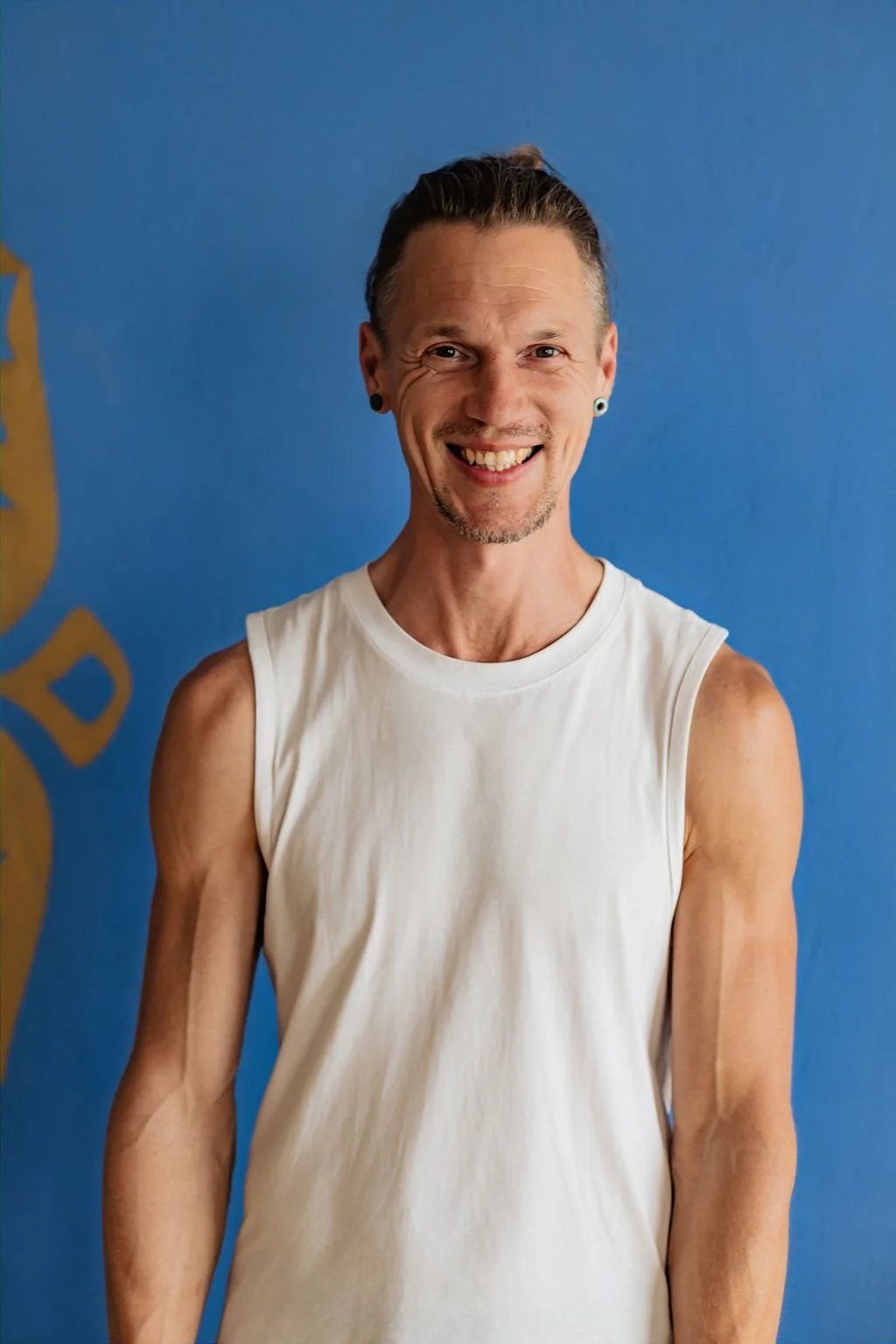 Paulo smiling to the camera with his hair back and a white muscle shirt.