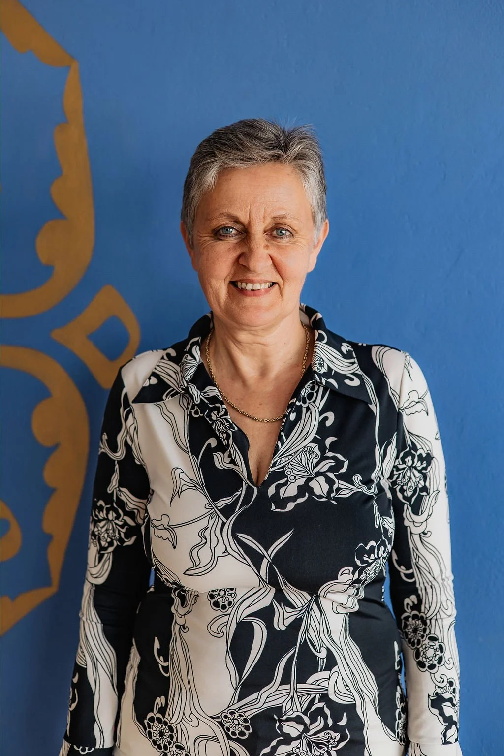 Karuna, wearing a white & black blouse. She smiles to the camera to welcome her massage clients