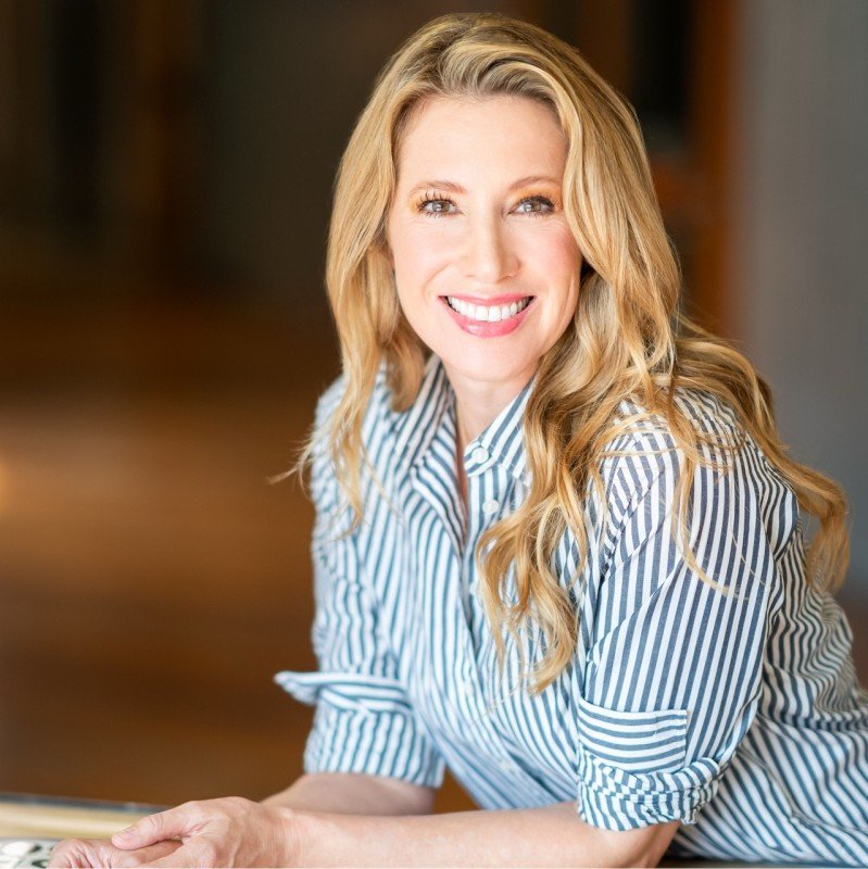Woman with long blonde hair wearing a blue and white striped shirt, smiling at the camera.