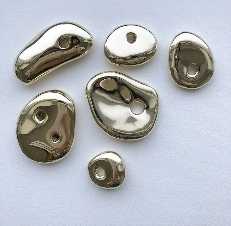 Seven shiny metallic beads with holes, irregular shapes, on a white background.