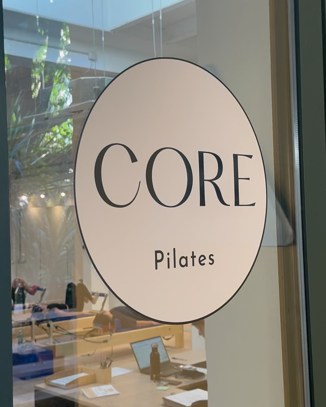 Segno su una porta con la scritta "CORE Pilates" e una finestra attraverso la quale si vedono persone che fanno esercizi di Pilates in un'aula.