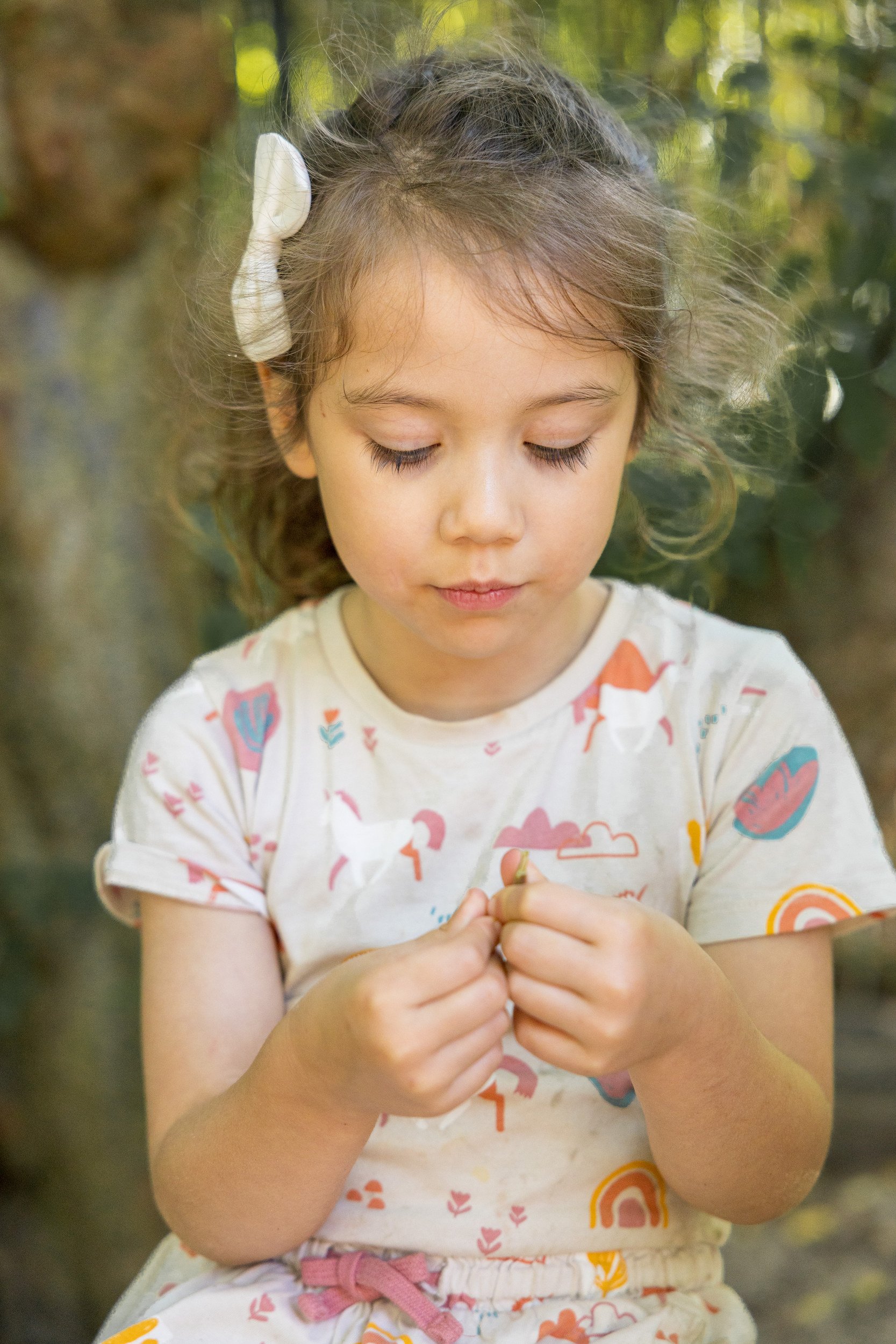 Kind mit lockigen Haaren sitzt draußen im Grünen – authentische Kinderfotografie im Kita-Alltag.