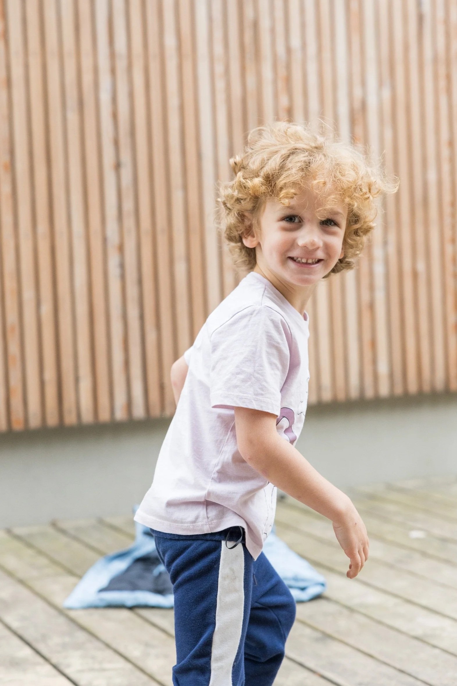 Lachender Junge auf einer Holzterrasse – natürliche Kinderfotografie draußen im Grünen.