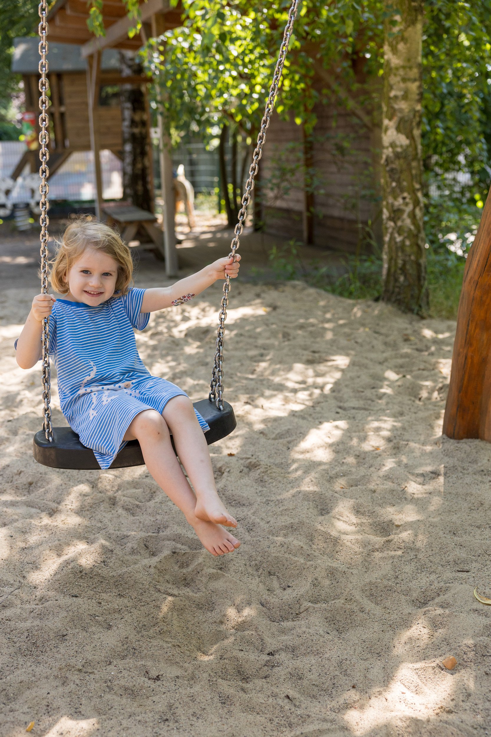 Mädchen schaukelt im Sand auf dem Spielplatz – natürliche Momentaufnahme aus dem Kita-Alltag.