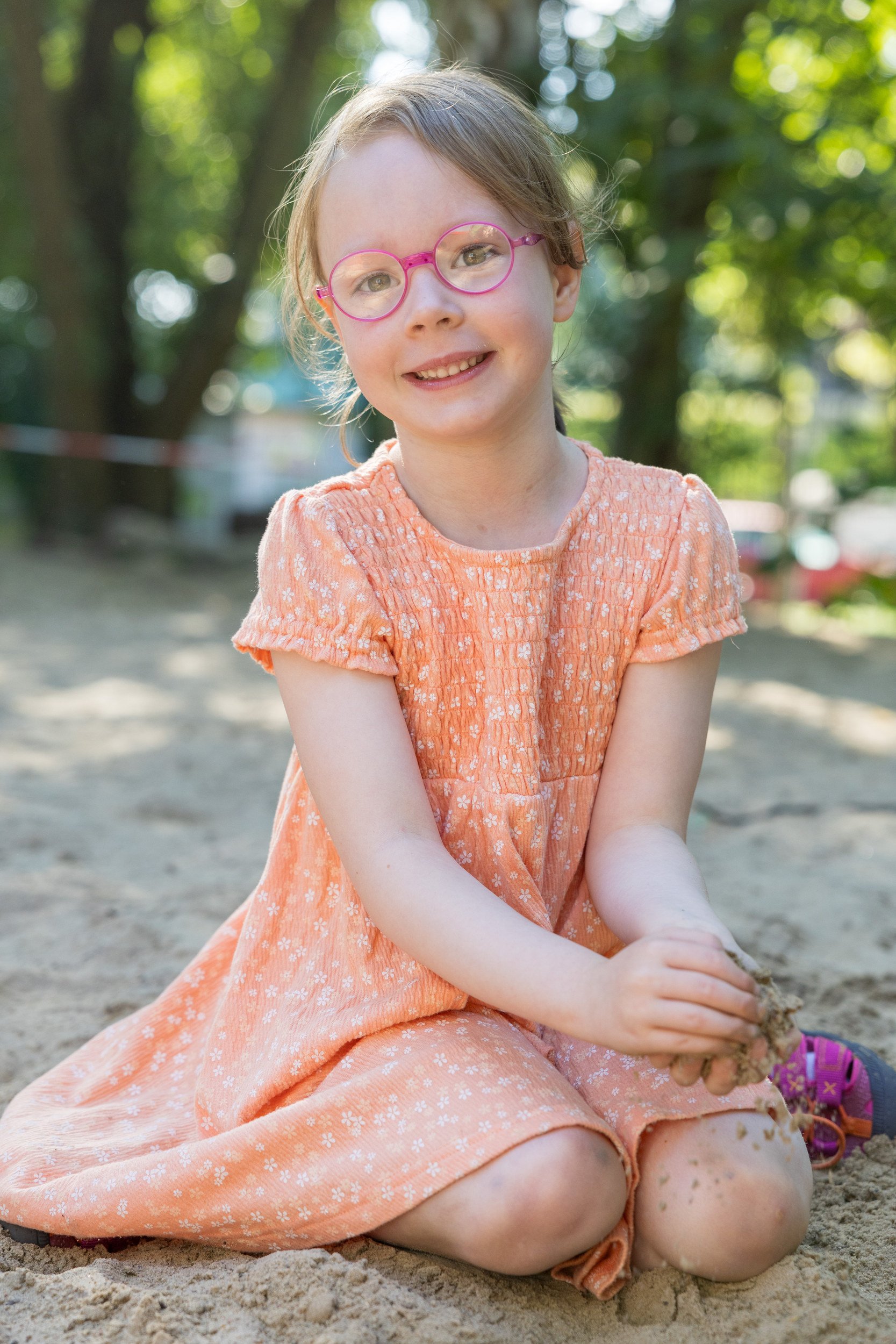 Mädchen mit Brille spielt konzentriert im Sand – authentische Fotografie aus dem Kita-Alltag.