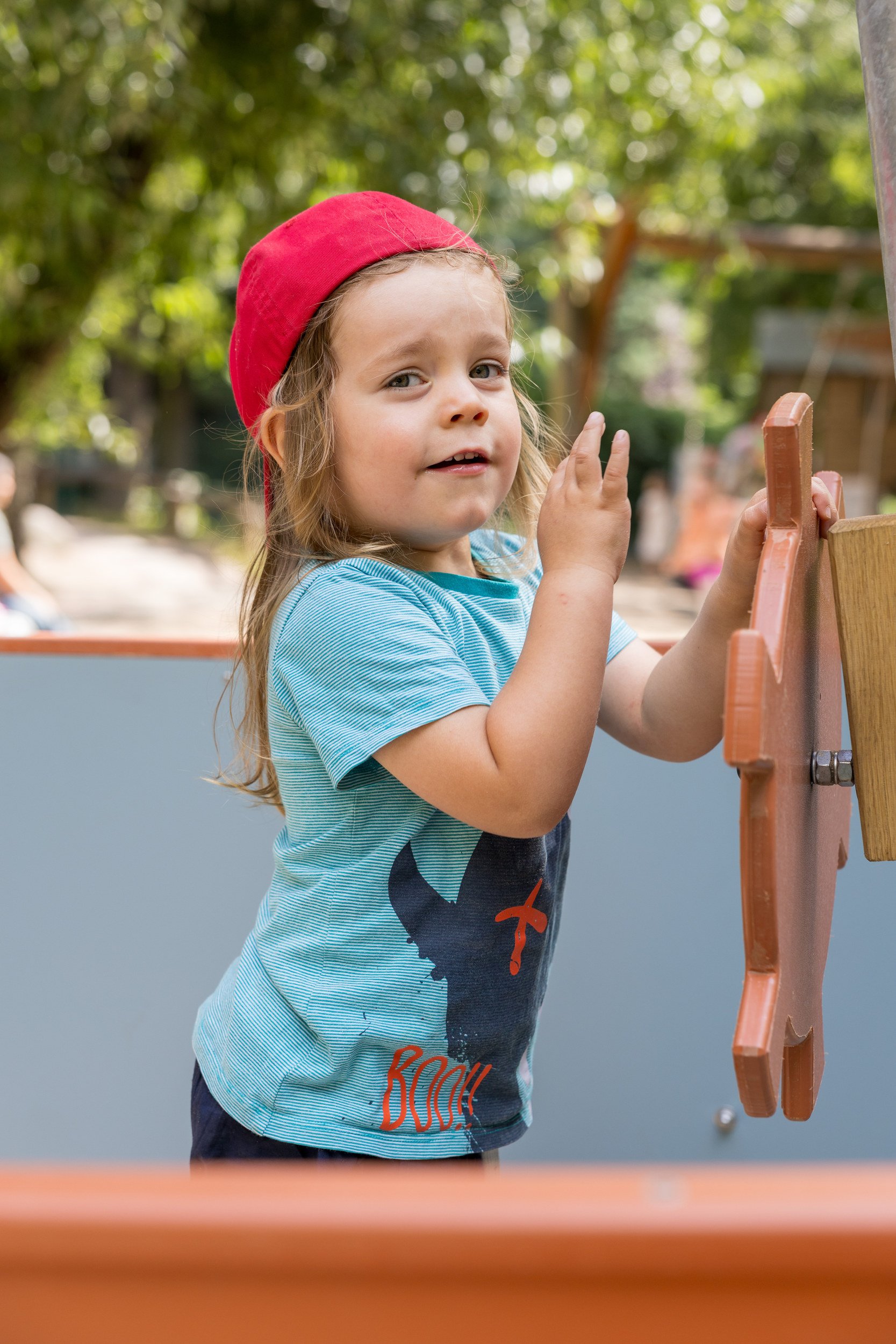 Junge mit roter Mütze spielt draußen – natürliche Kinderfotografie auf dem Spielplatz.