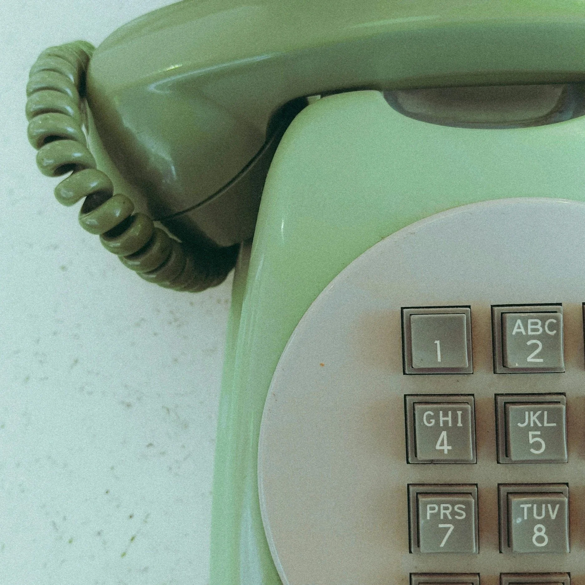 Close-up of a vintage rotary telephone and a portion of an old calculator with keys labeled 'ABC', '123', and other characters, on a speckled white surface.