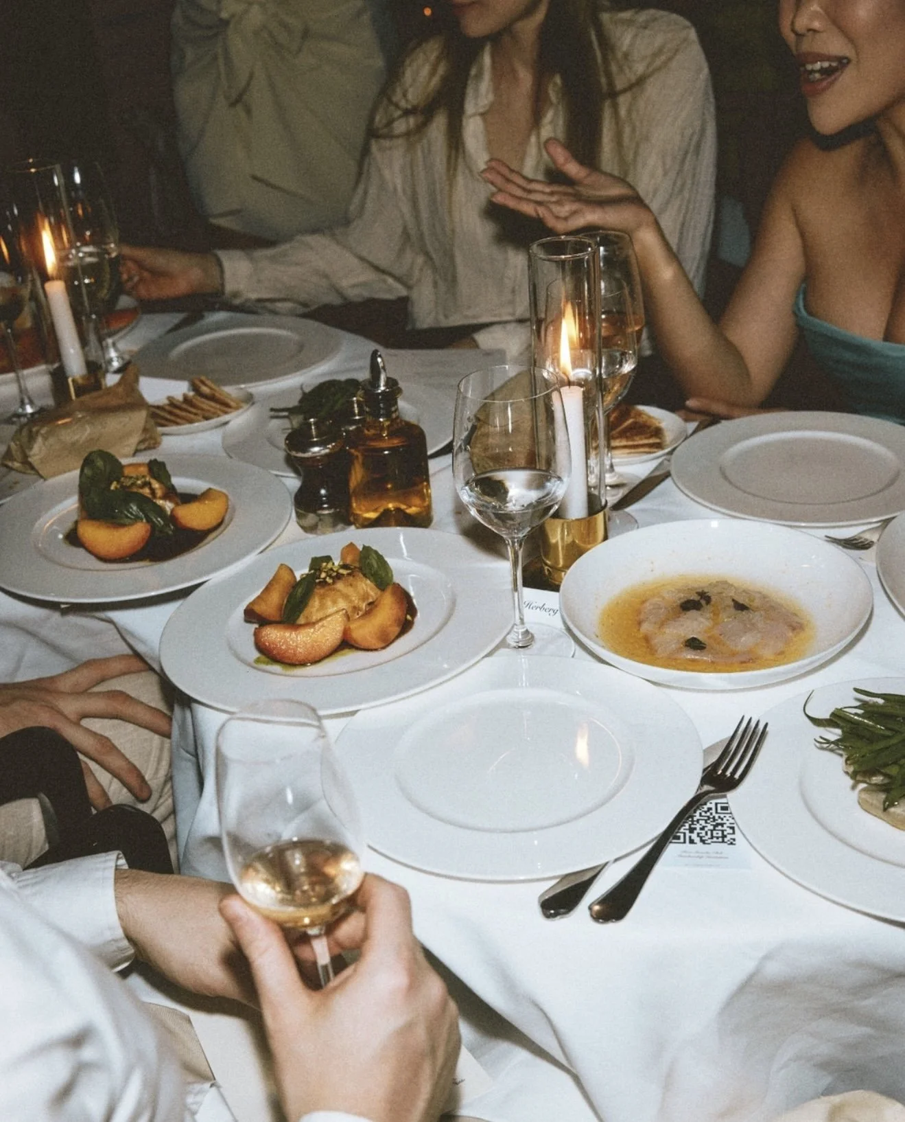 A dinner table set with plates of food, glasses of wine, and candles, with people engaging in conversation.