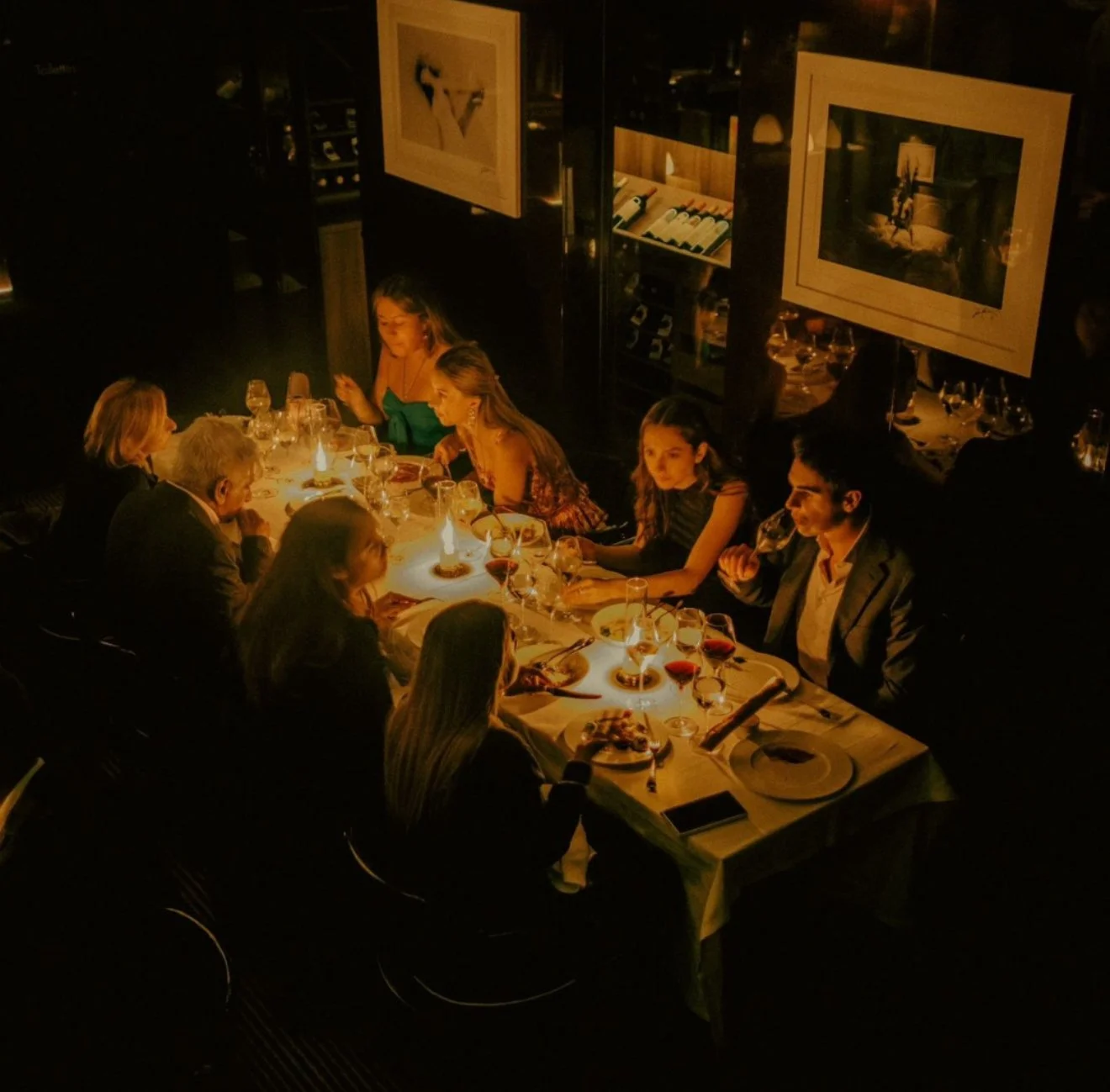 A group of people dining at a restaurant table illuminated by candlelight, enjoying wine and conversation.