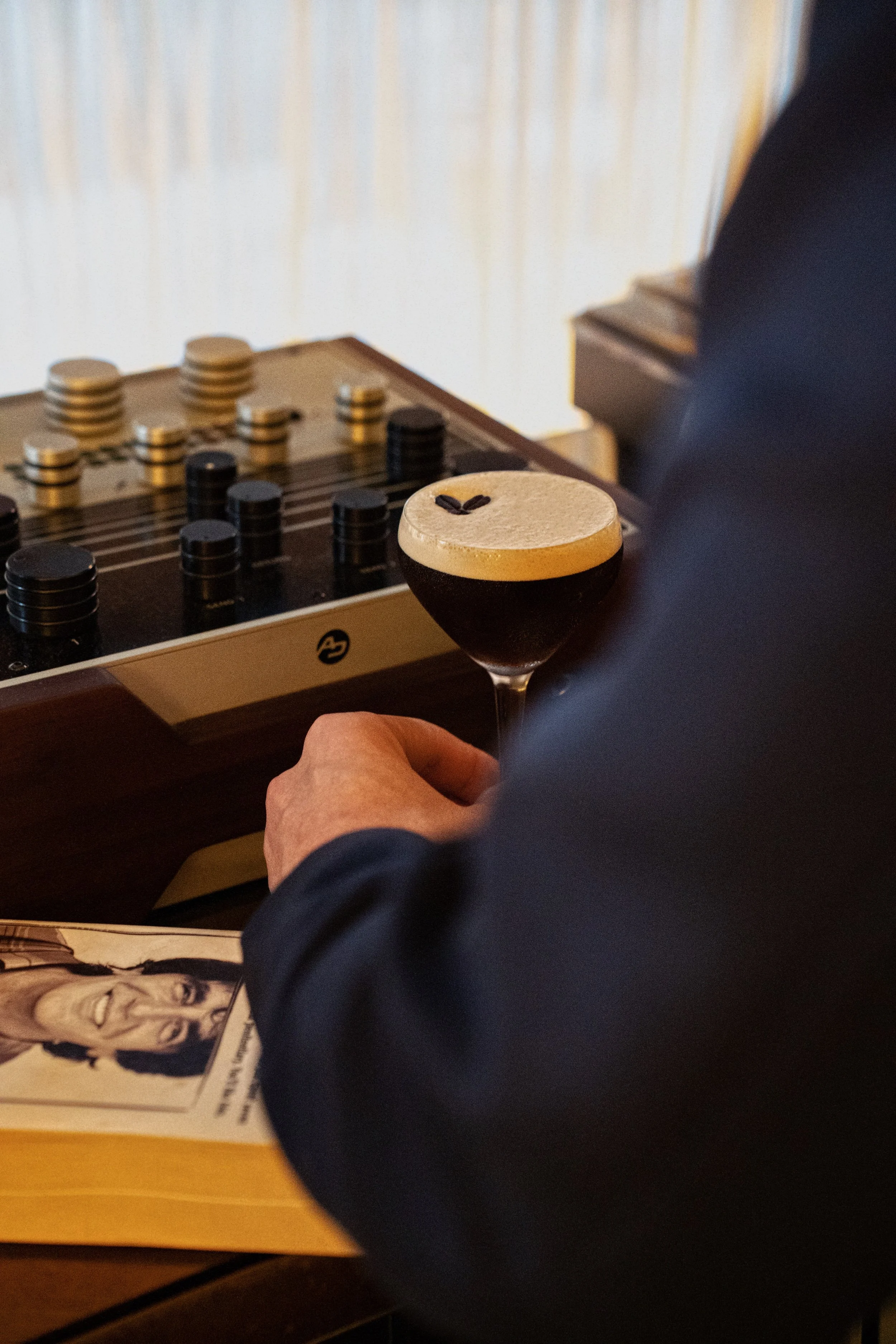 Person playing chess next to a drink with foam and coffee beans on top.