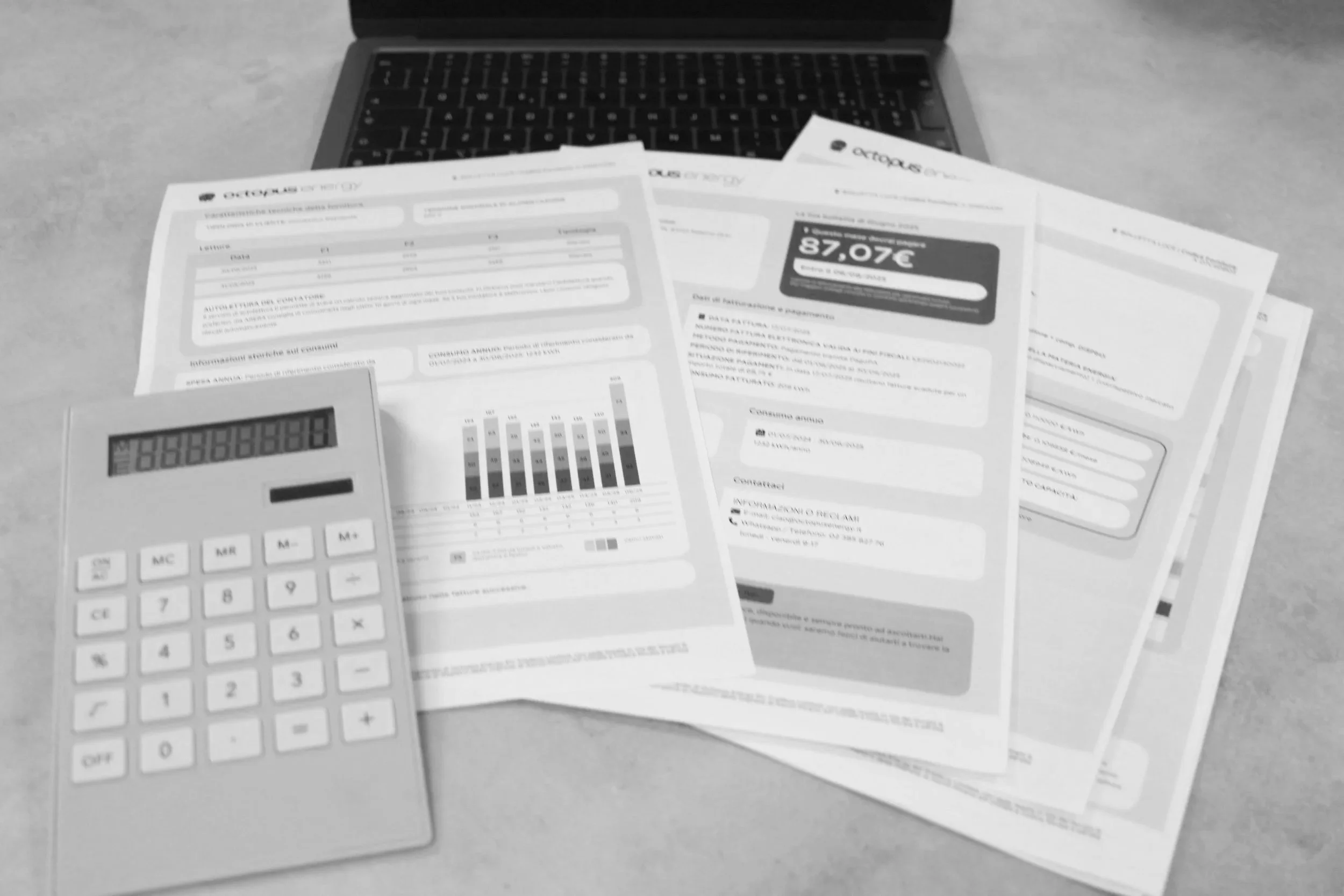 A calculator and multiple sheets of paper with graphs and text on a desk in front of a closed laptop.