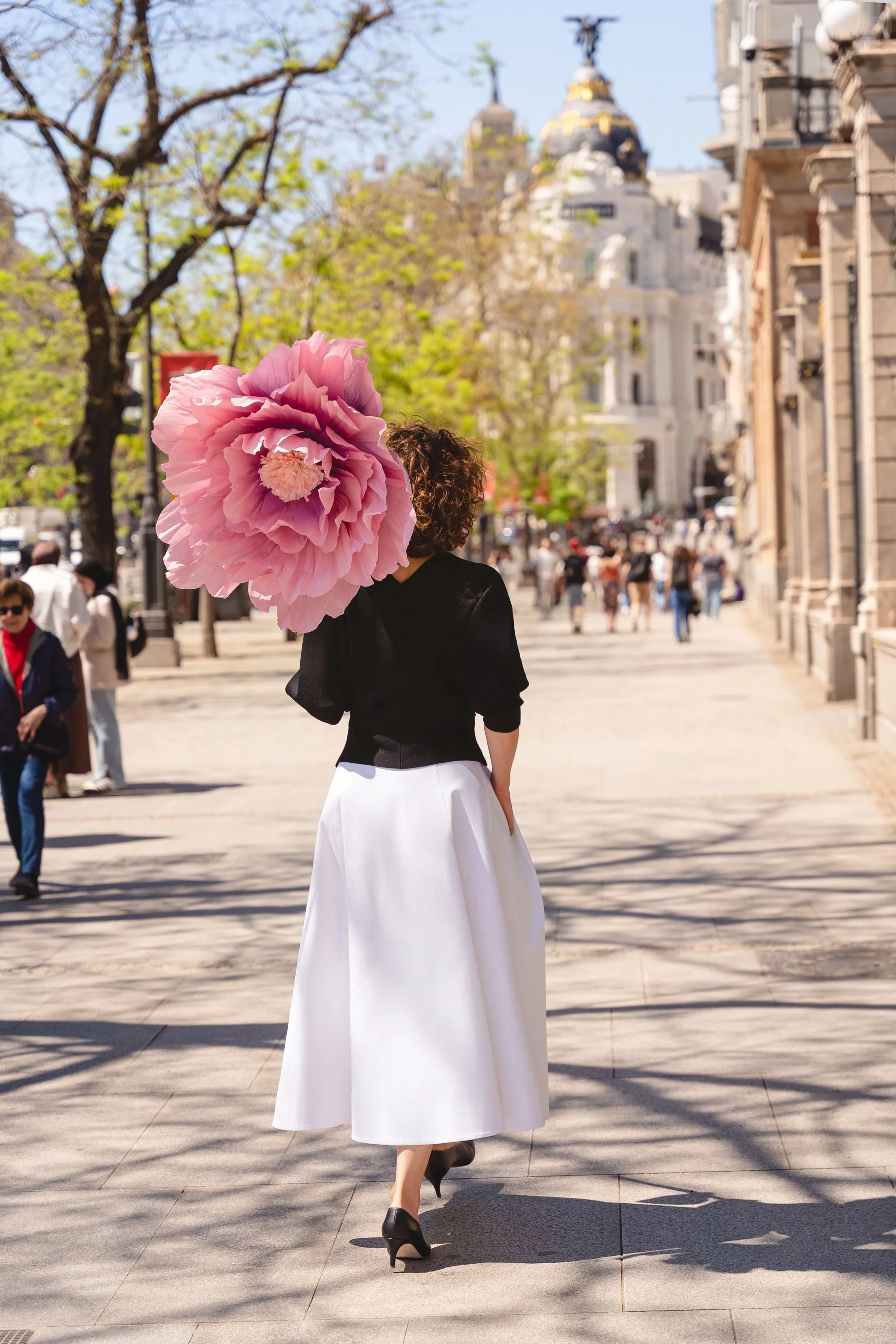Coach Peony Path Coaching spacerująca po Gran Via w Madrycie z dużym różowym kwiatem
