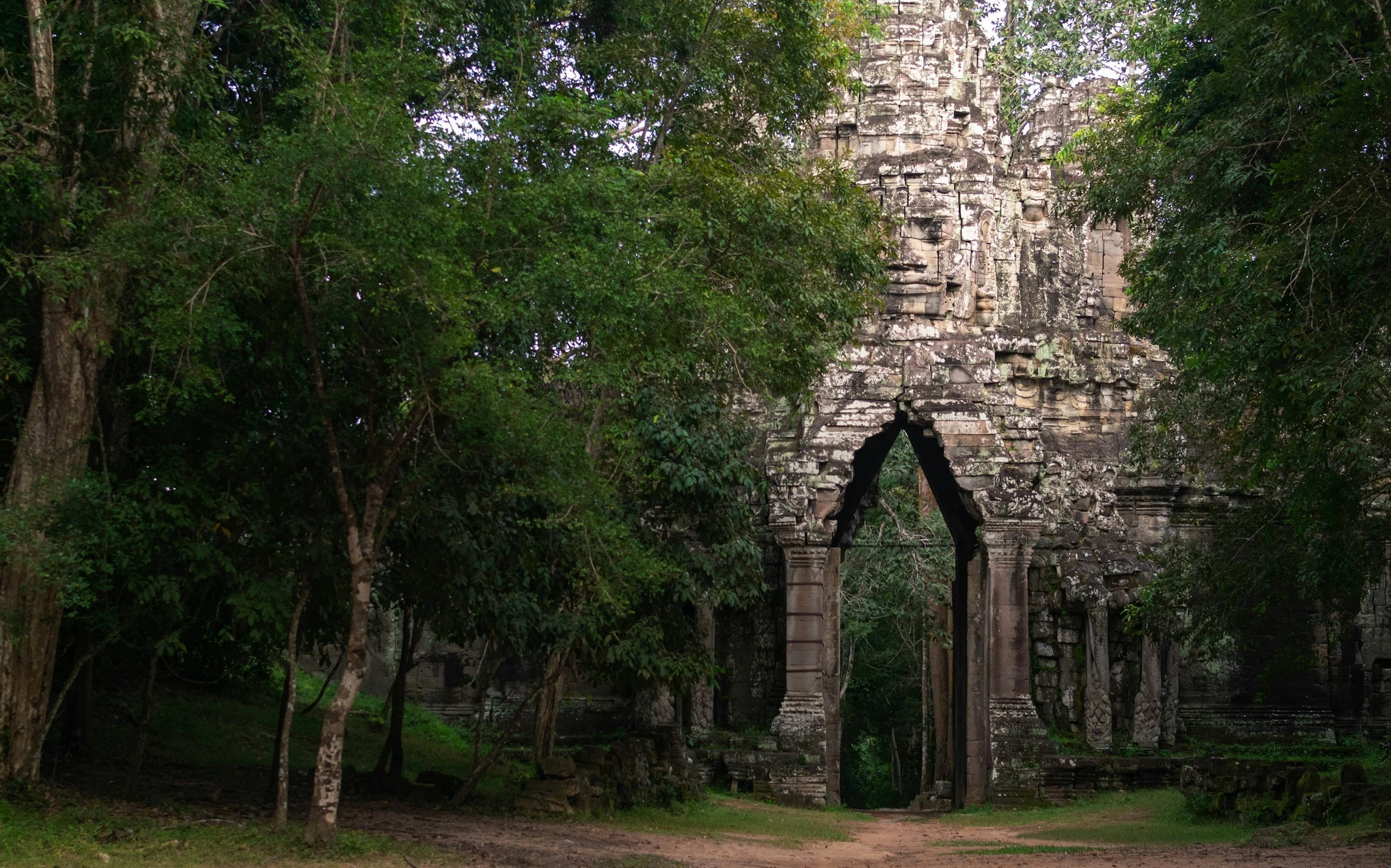 An ancient stone temple ruin partly covered by dense green foliage in a jungle setting.