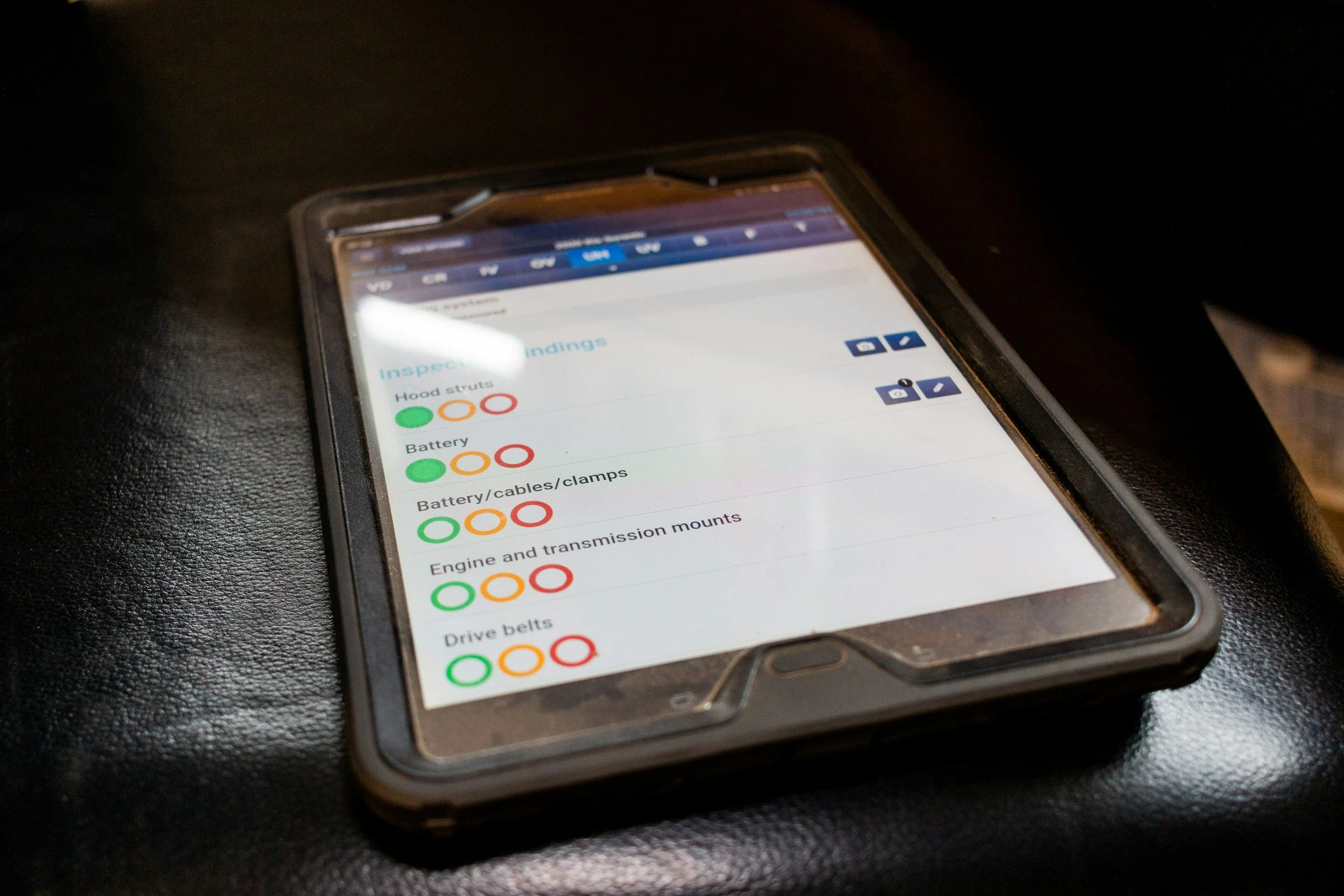 A smartphone lying on a black surface displaying a vehicle inspection checklist with colored indicators for various vehicle parts.