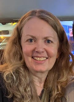 A smiling woman with long curly hair in an indoor setting.