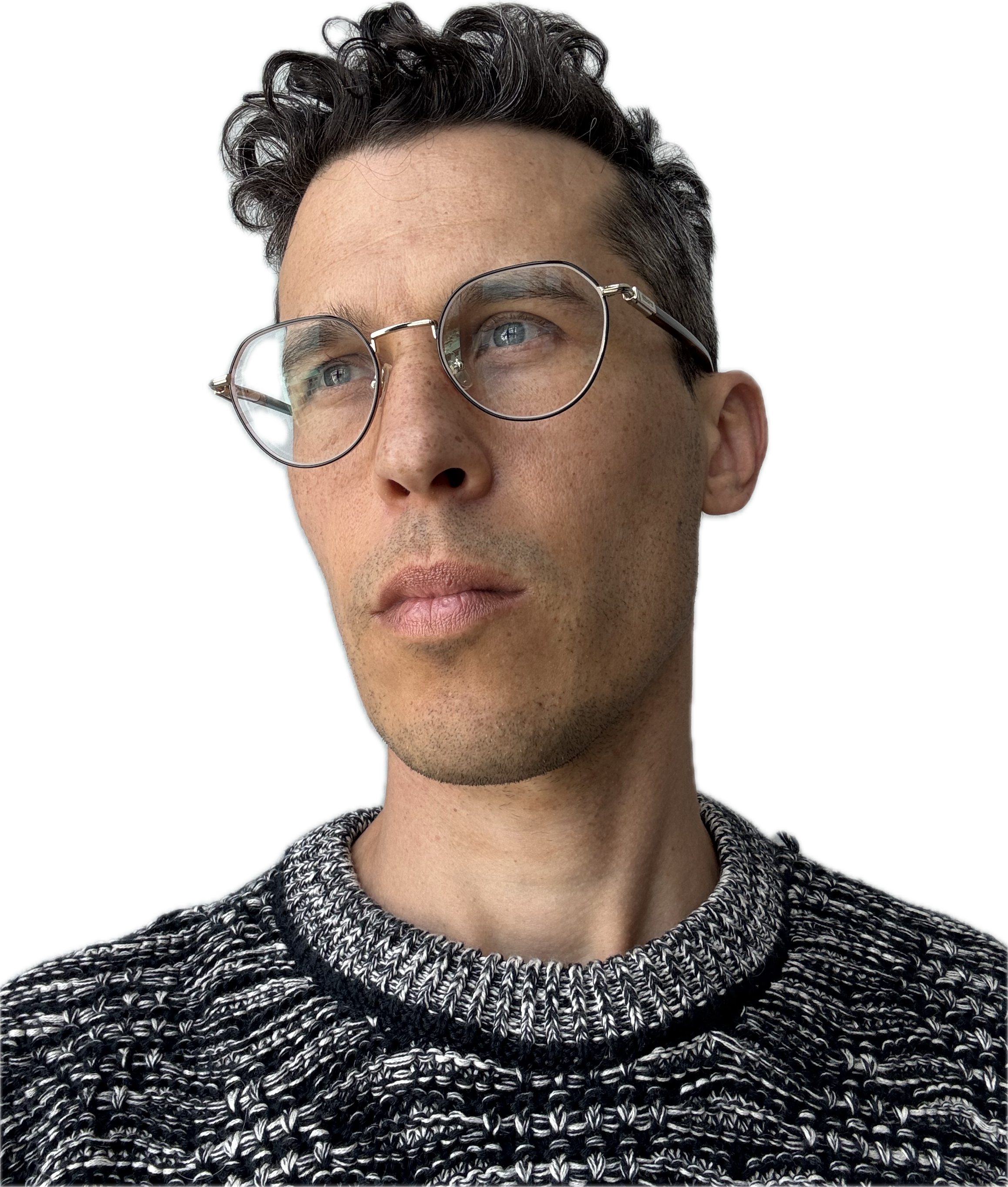 Close-up of a young man with dark curly hair and light skin, wearing glasses and a black and white knitted sweater, looking to the side.