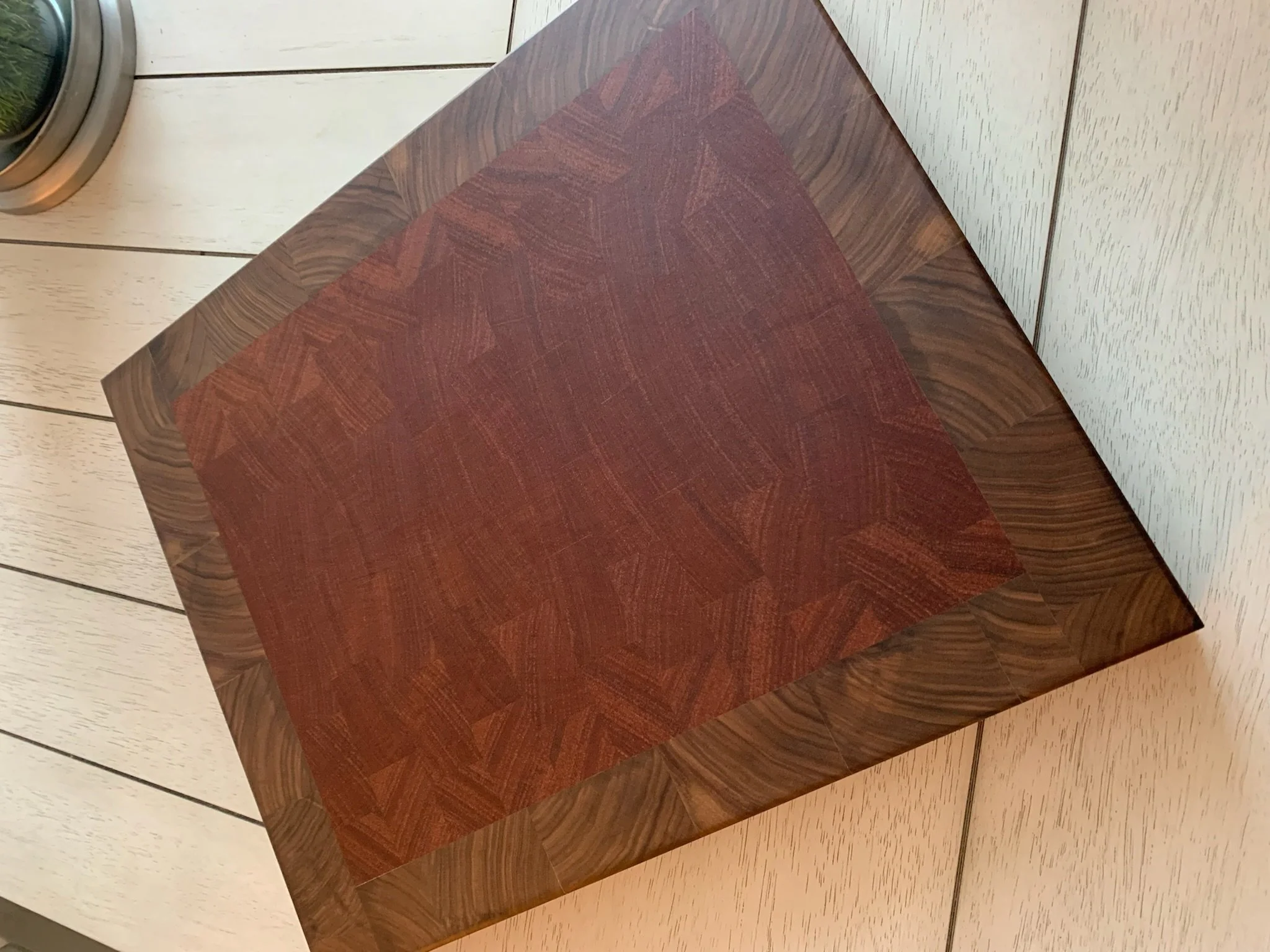 A wooden table with a dark finish and a red cloth on top, placed on light-colored wooden flooring with a white wall behind.