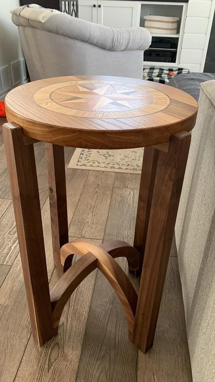 A wooden round side table with a compass rose design on the top surface, placed in a living room area.