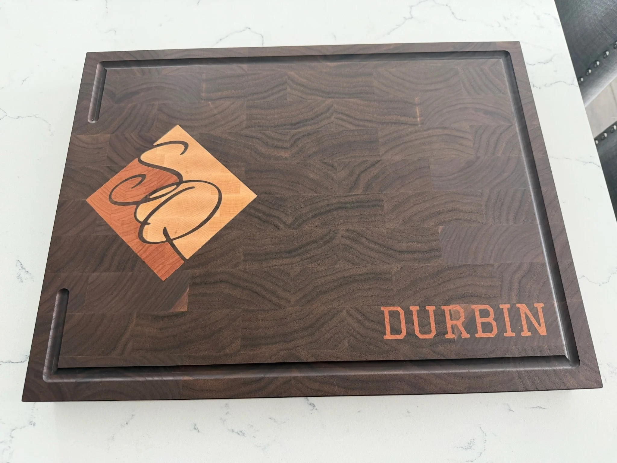 Wooden cutting board with a small orange paper label showing black cursive text and the word 'DURBAN' written underneath in orange capital letters.
