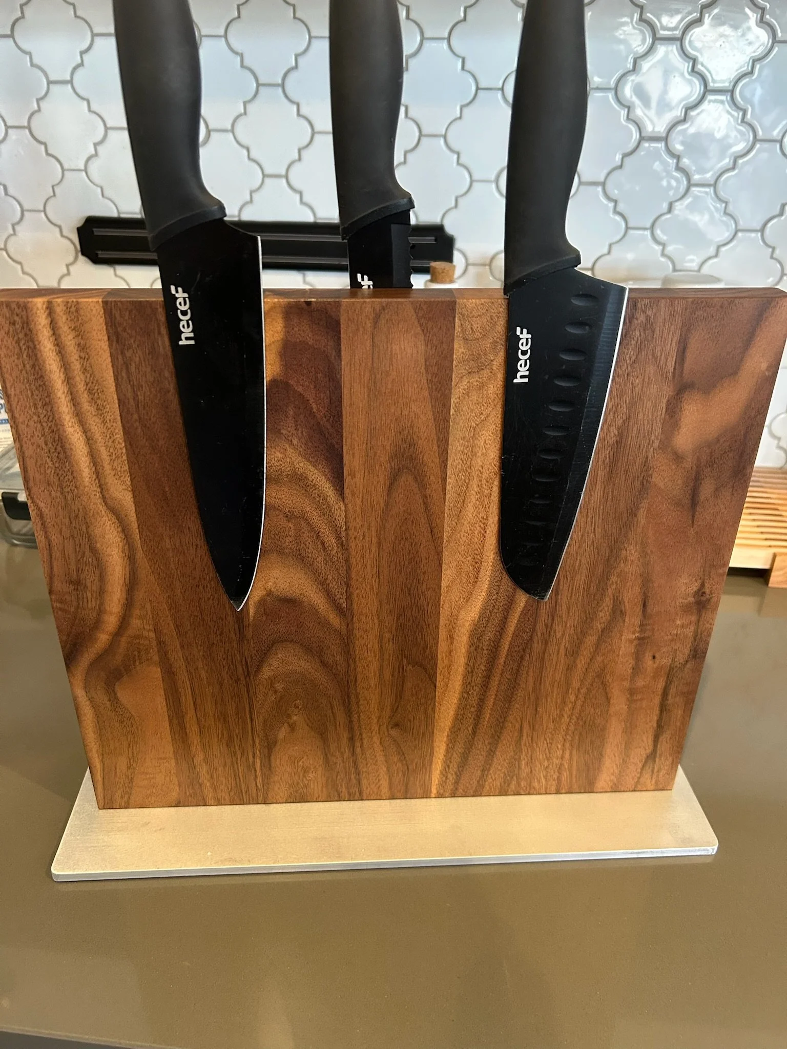 Two black kitchen knives inserted into a wooden knife block on a kitchen counter with a tiled backsplash in the background.