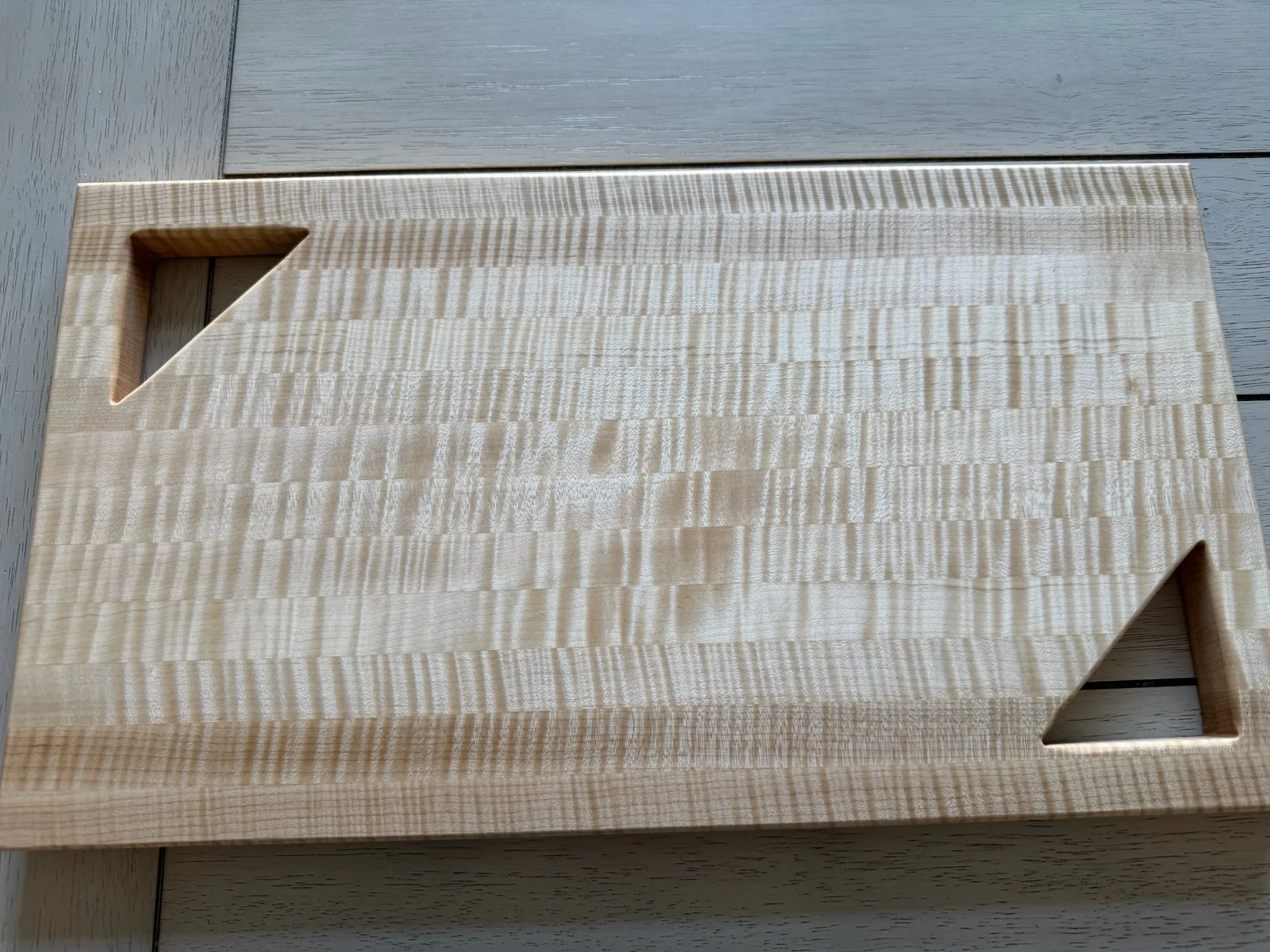 A rectangular wooden object with a large cutout in the top left corner, placed on a light-colored wooden surface.